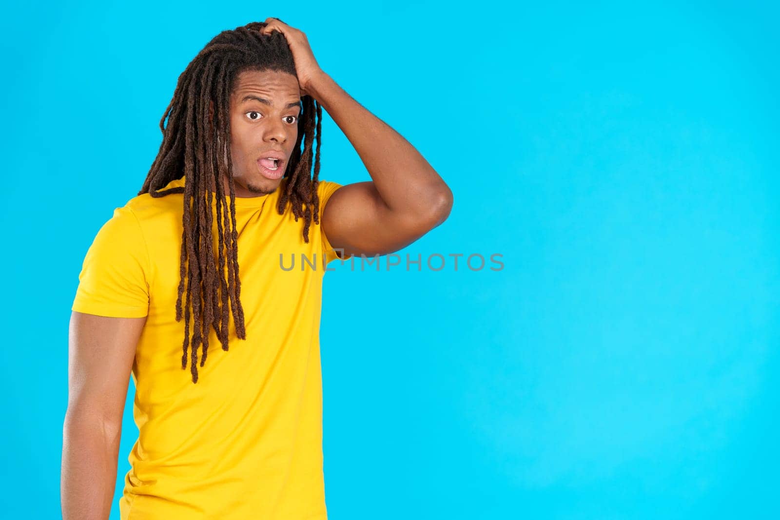 Man with dreadlocks with hand on face and thoughtful expression in studio with blue background