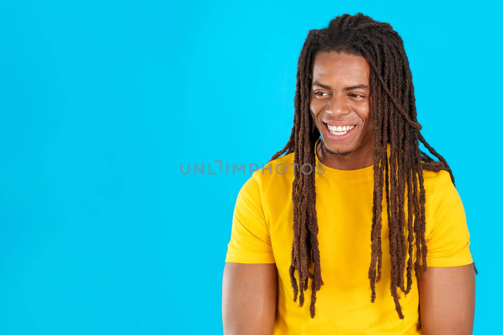 Distracted smiley latin man with dreadlocks in studio with blue background