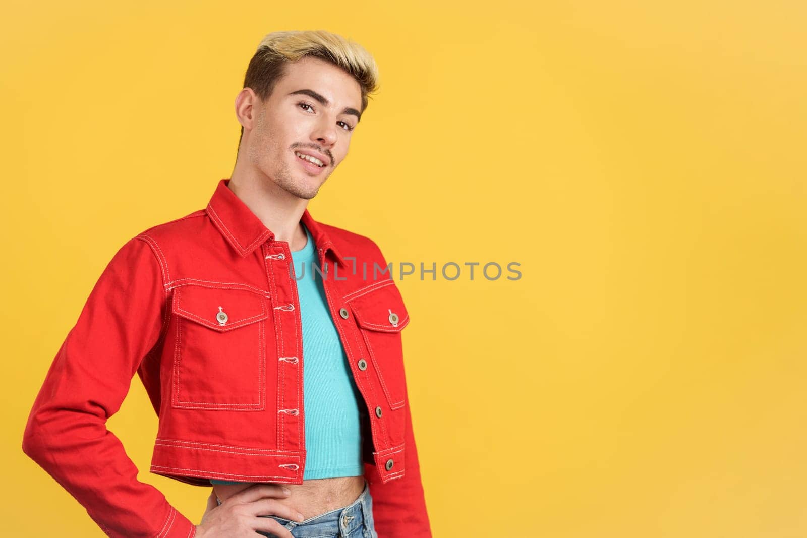 Caucasian gay man in colorful clothes smiling at the camera in studio with yellow background