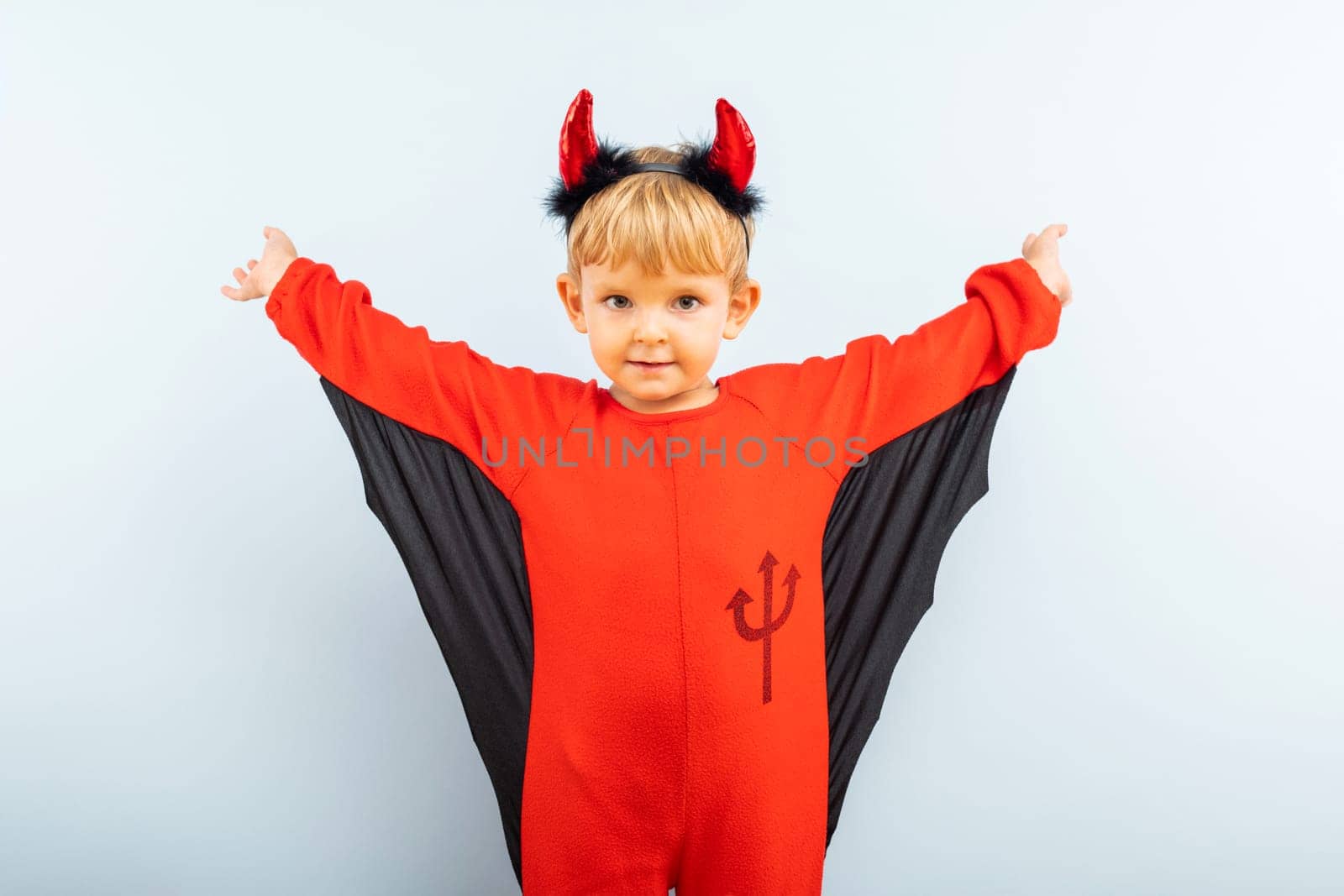 Happy Halloween. Cute little boy in devil halloween costume with horns on light blue background.