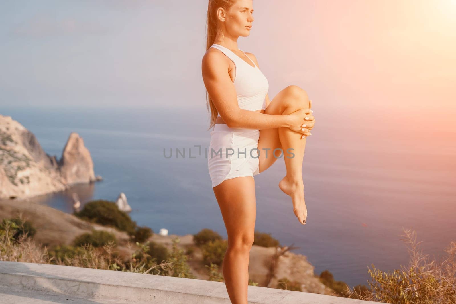 Fitness woman sea. A happy middle aged woman in white sportswear exercises morning outdoors in a park with a beach view. Female fitness pilates yoga routine concept. Healthy lifestyle. by panophotograph
