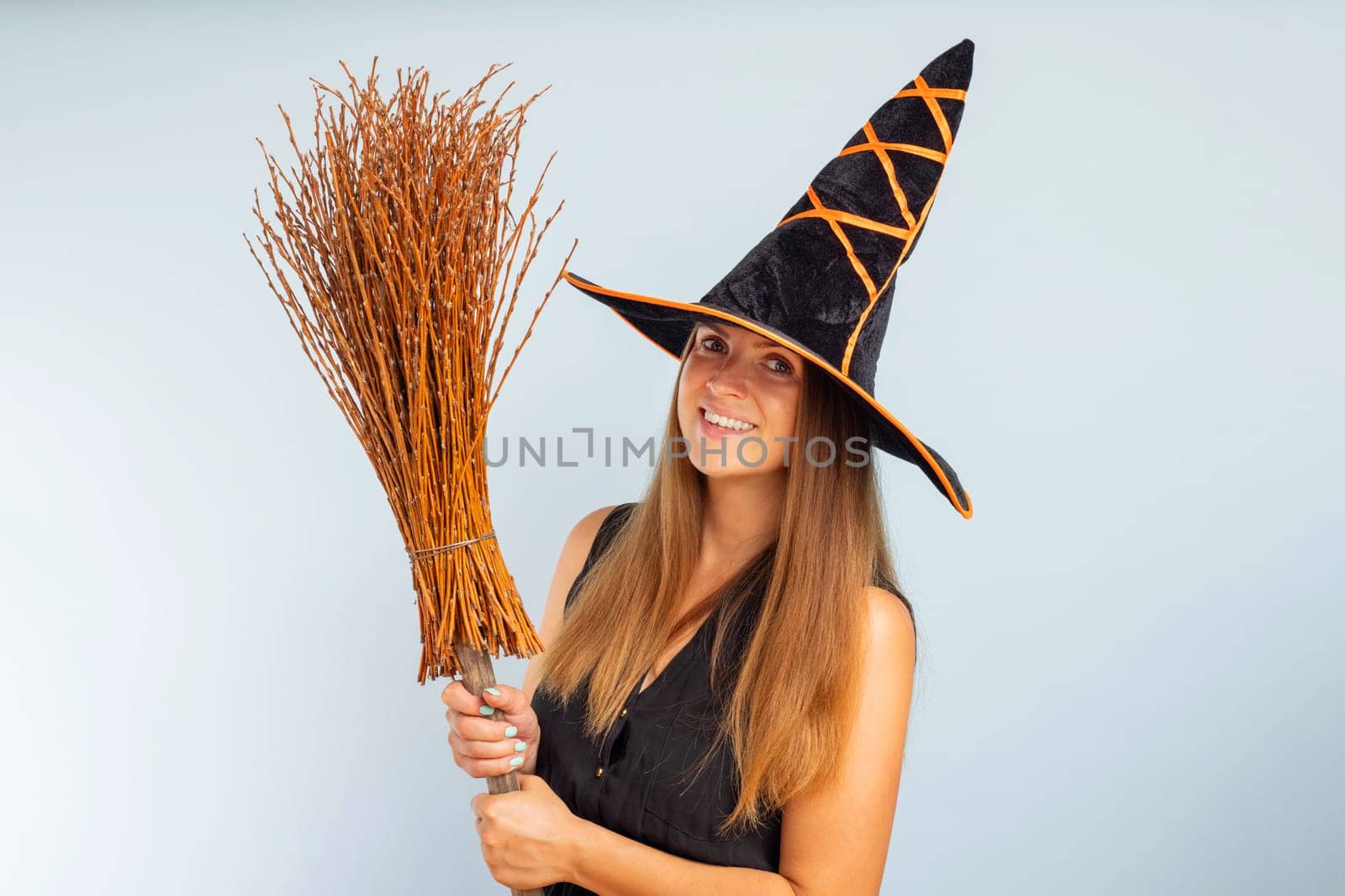 Happy Halloween. Happy young woman in halloween witch costume with broom on a light background. Halloween party concept.