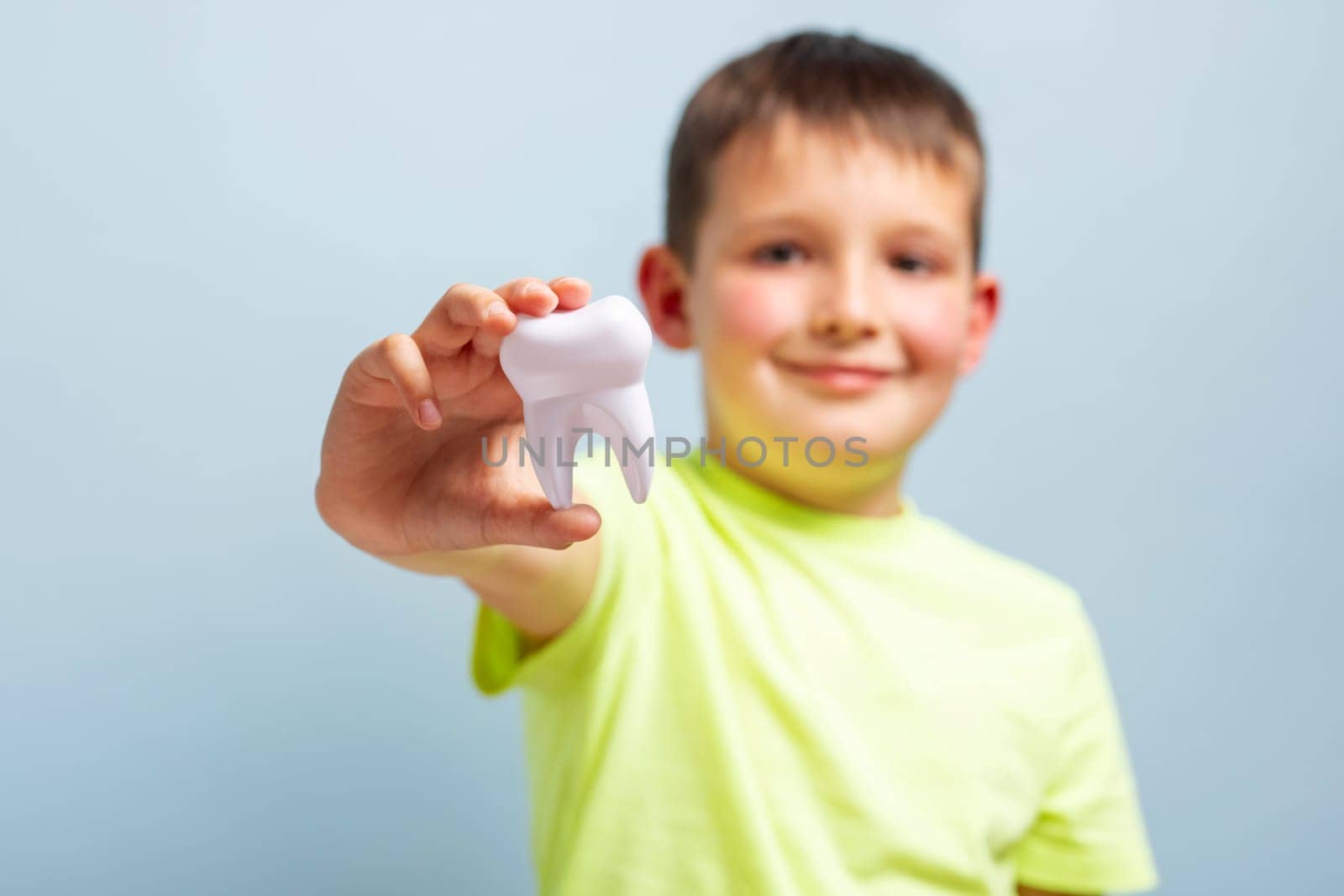 Child holds big white toy tooth on a blue background. Caring for teeth. Dentistry and healthcare concept. Healthy teeth concept.