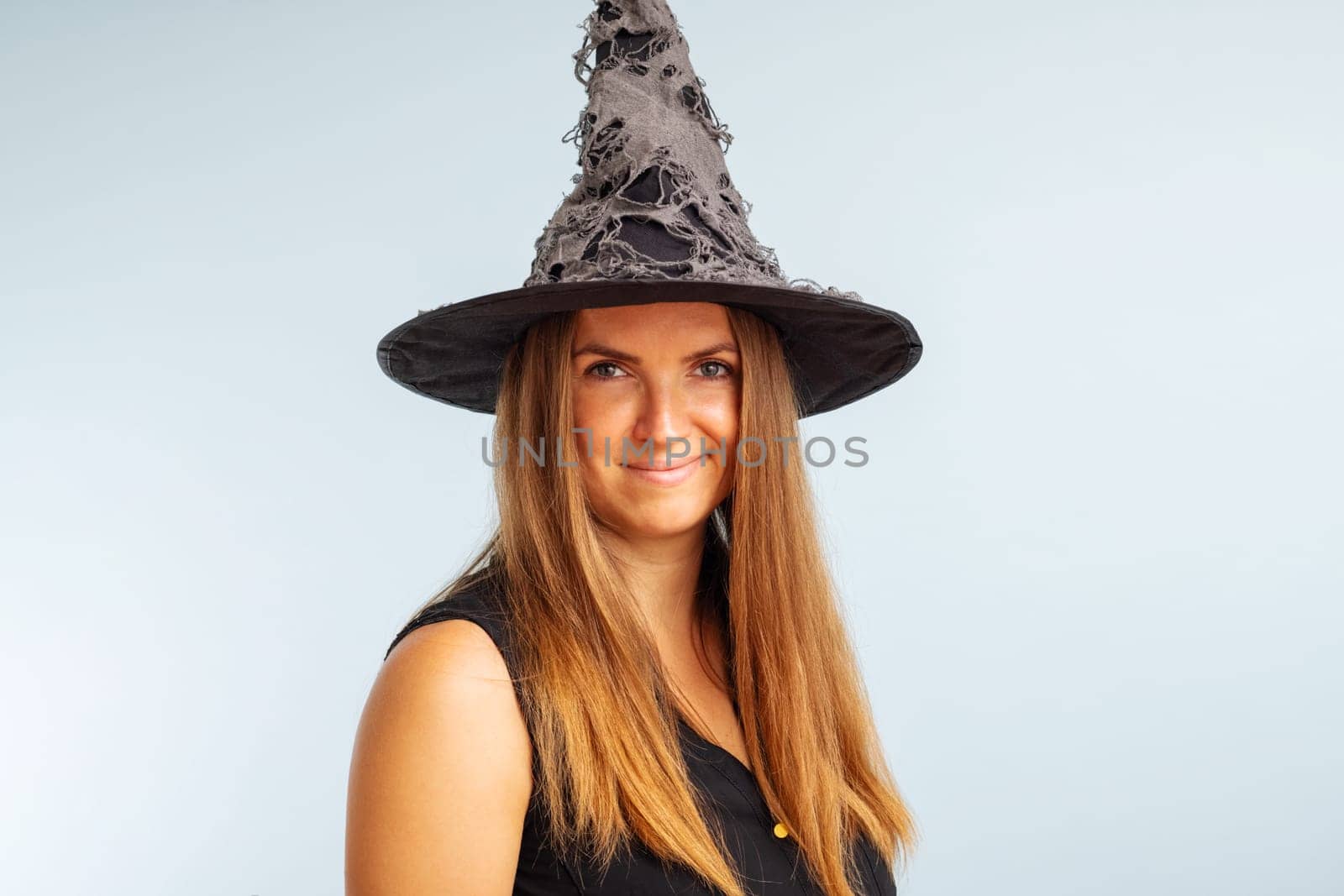 Happy Halloween. Happy brunette woman in halloween witch costume with black hat on a light background.