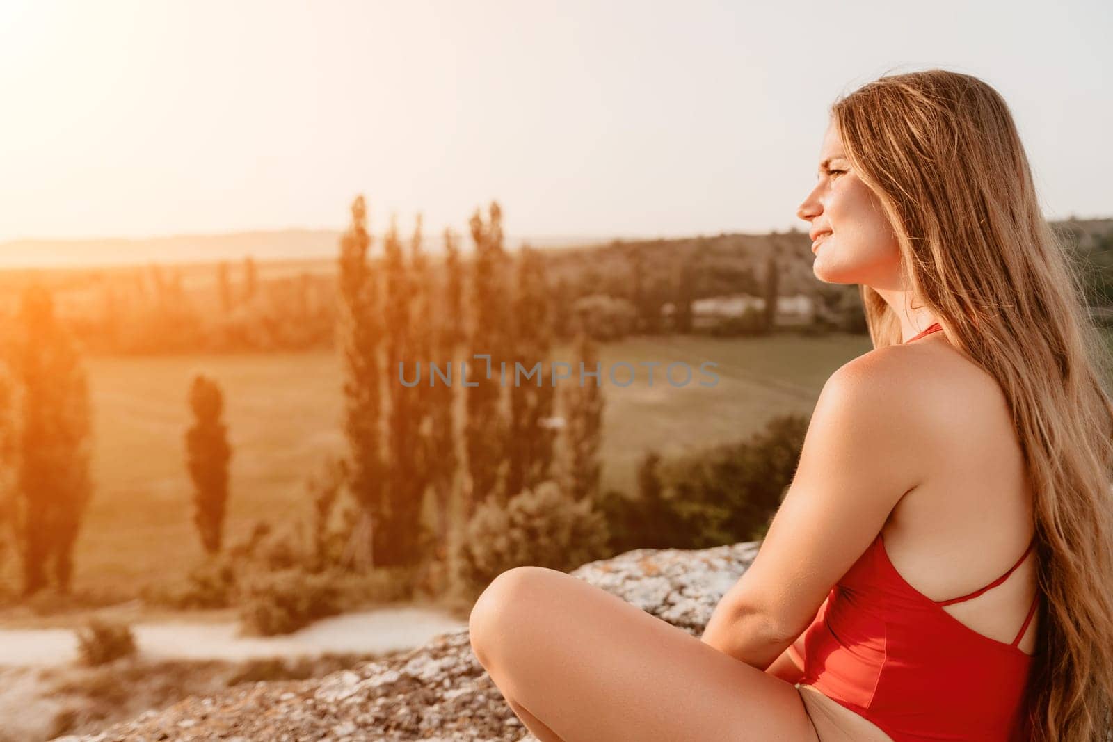 Well looking middle aged woman with long hair, fitness instructor in leggings and tops doing stretching and pilates on the rock near forest. Female fitness yoga routine concept. Healthy lifestyle by panophotograph