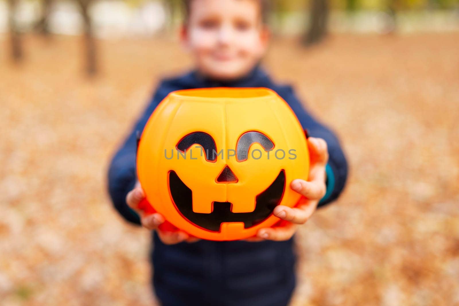 Child holds bucket shaped like a halloween pumpkin jack o lantern in park by andreyz