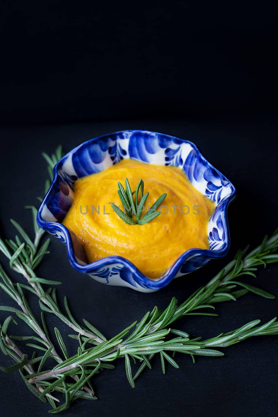 delicious pumpkin cream soup and black background with rosemary.