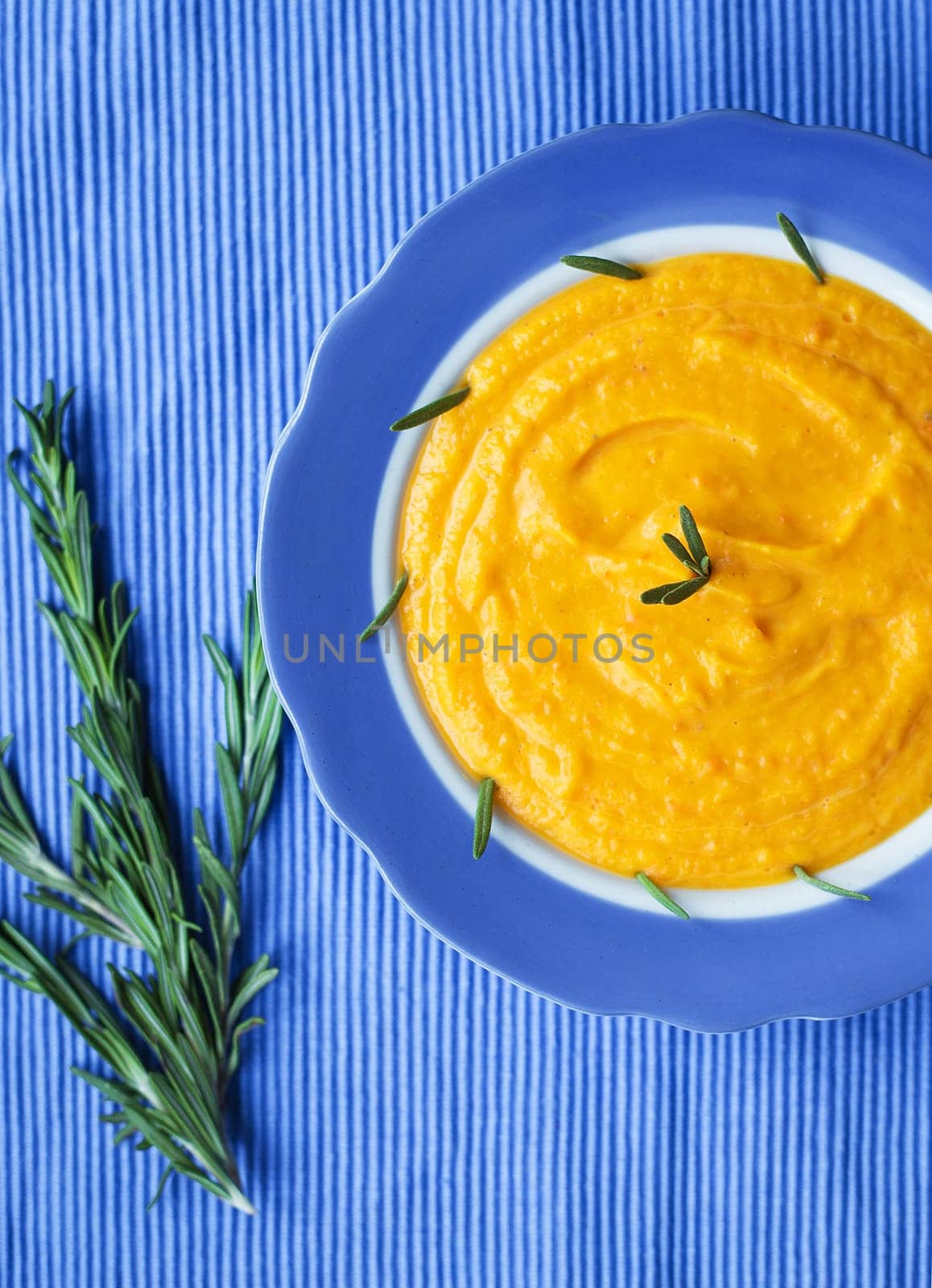 pumpkin cream soup in a blue plate on blue napkin, a branch of rosemary.