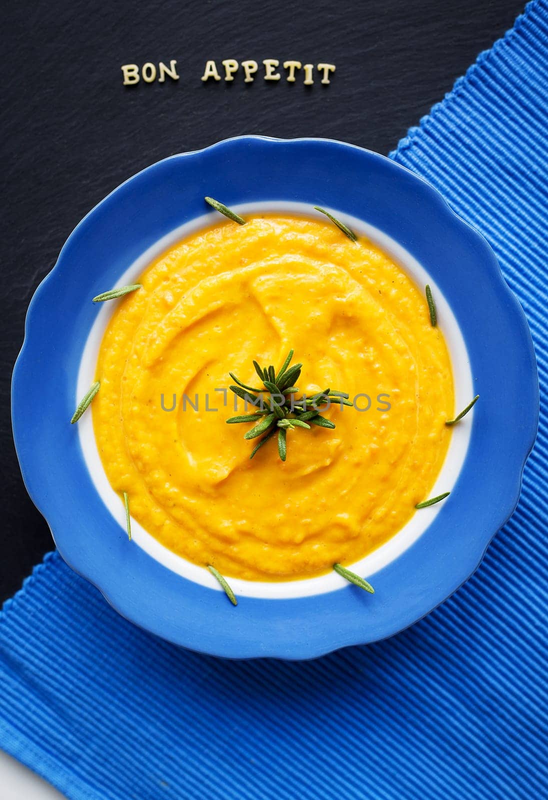 pumpkin soup in a blue plate on a black background with a blue cloth, close-up