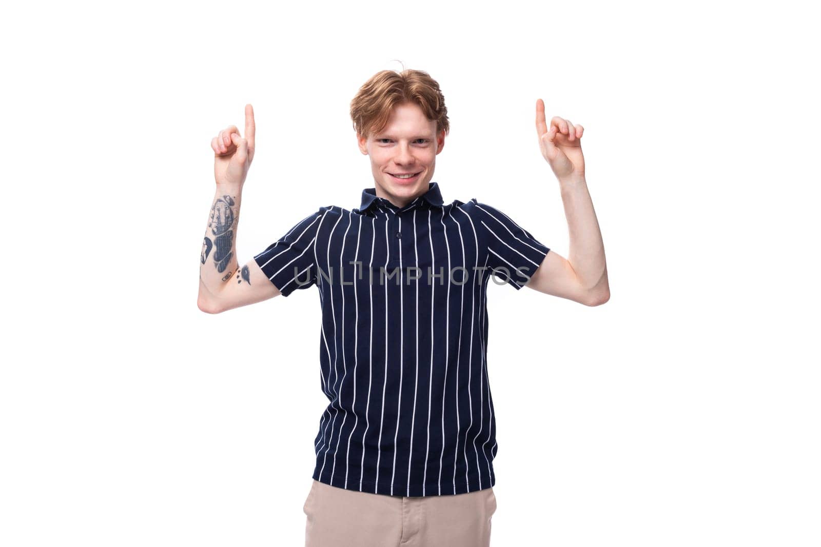 young European blond guy in a striped polo shirt with a tattoo shows his hand to the side on a white background by TRMK