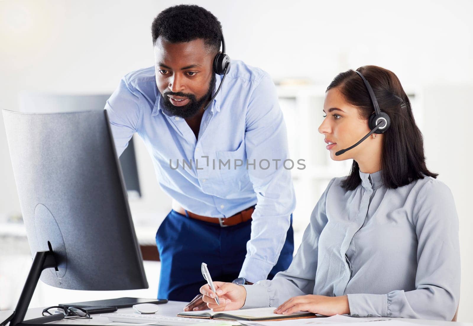 Collaboration, mentor helping with colleague and headset with computer at her desk of modern office. Teamwork or support, partnership or communication and black man with intern at her workspace.