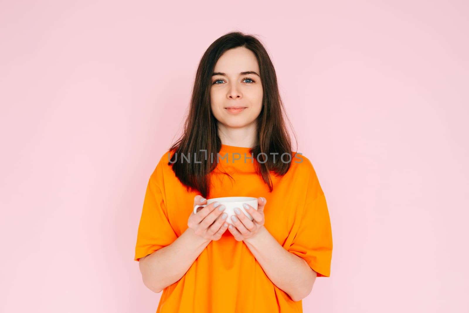 Serene Leisure: Charming Woman in Orange Attire, Savoring a Delightful Drink in a Mug - Relishing Free Time After Work, Tranquility and Bliss Isolated on Pink Background by ViShark