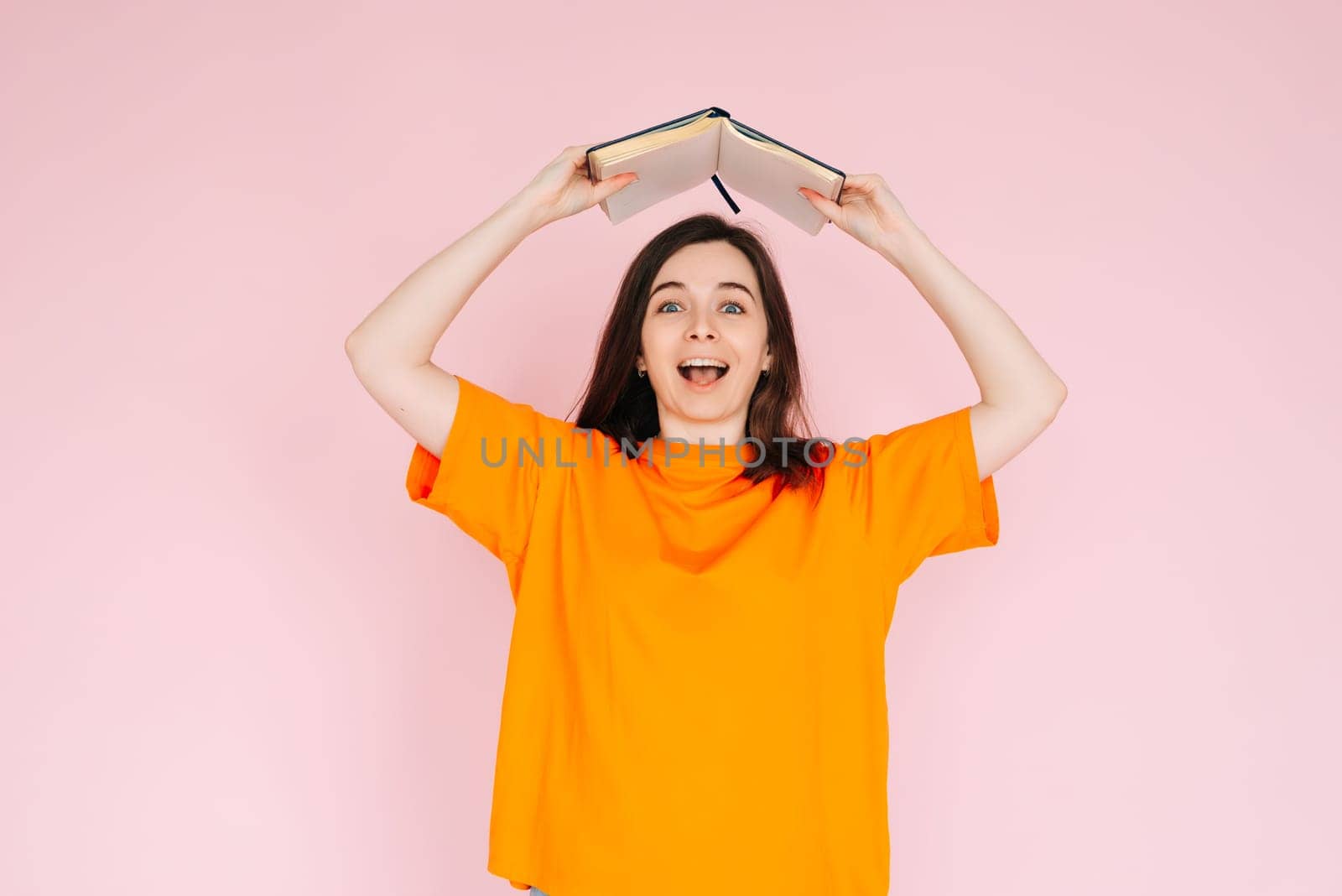 Joyful Book Enthusiasm: Cheerful Woman Holding Book Overhead with Exuberance - Delightful Mood and Positivity Concept, Isolated on Pink Background