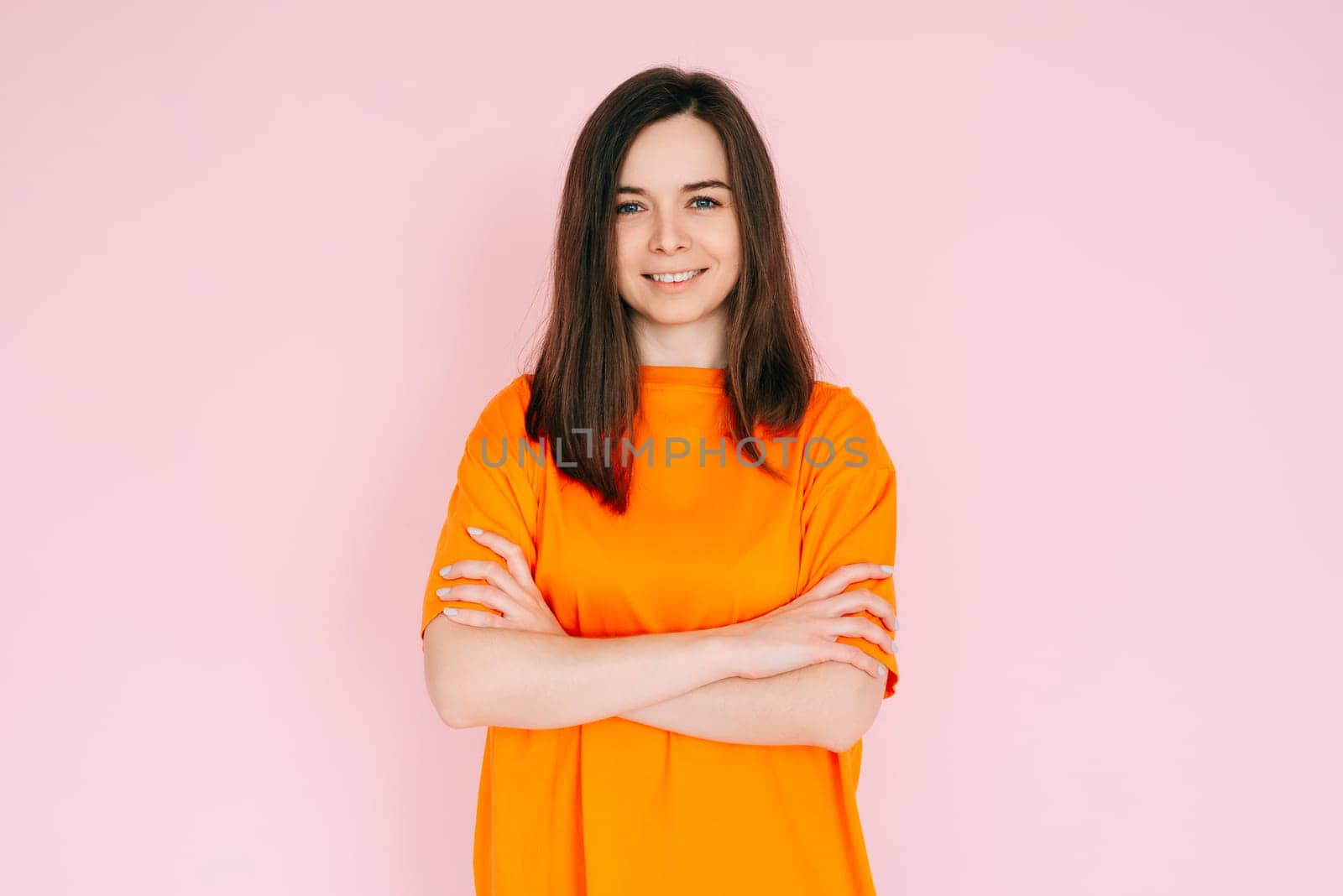 Radiant Joy: Beautiful Woman with Beaming Smile and Arms Crossed, Embracing Good Mood in Comfortable Attire - Vibrant Positivity on Pink Background.