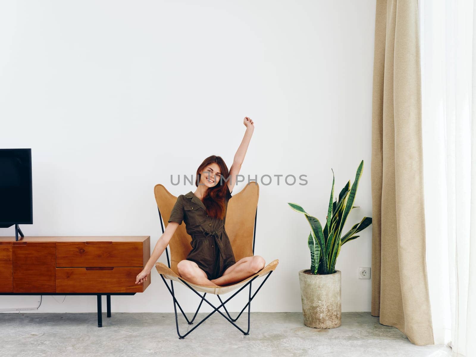 Woman sitting in a leather armchair near the window hands up smile , modern stylish interior Scandinavian lifestyle, copy space. High quality photo