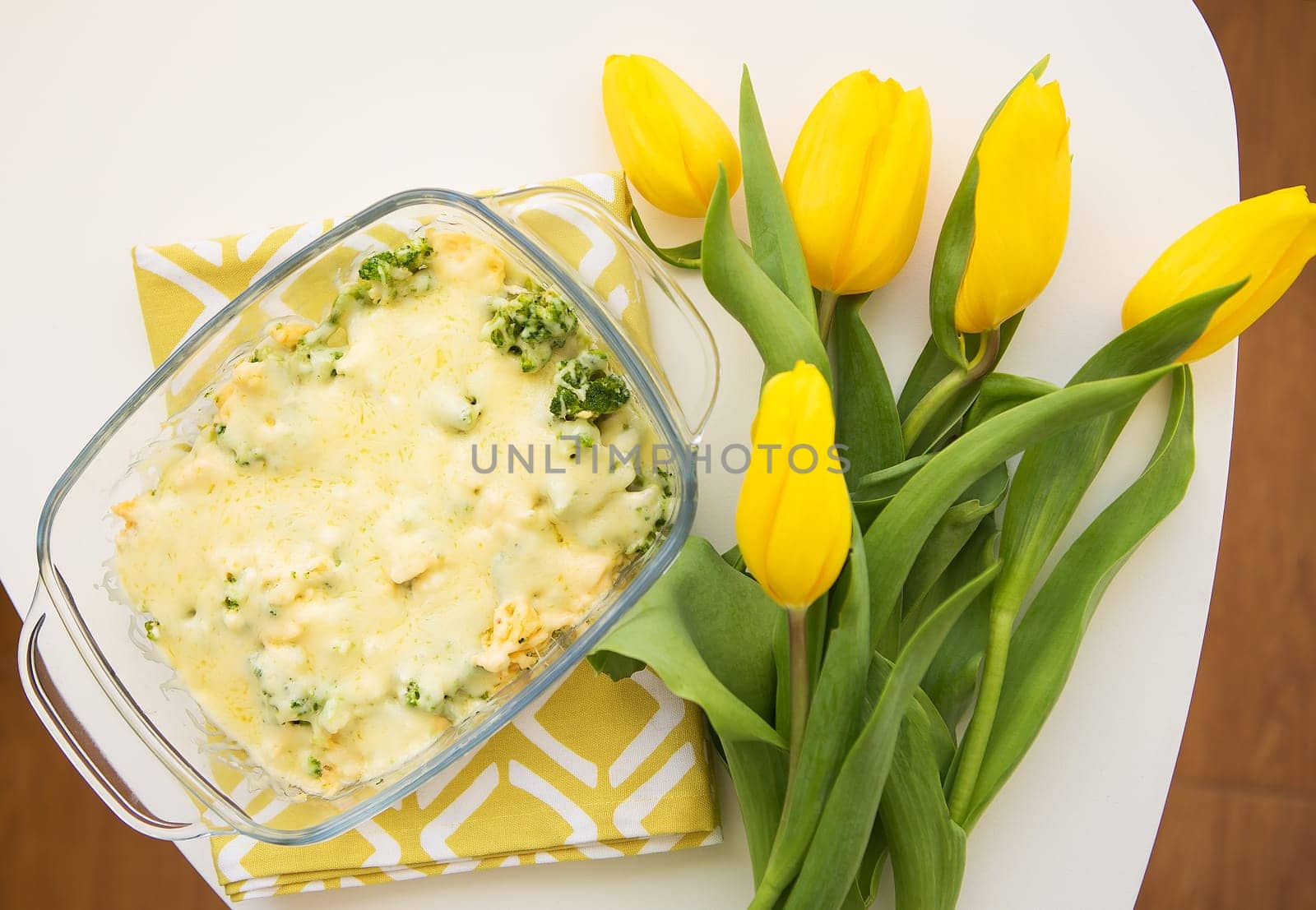 tasty casserole with broccoli, cheese and cream on a background of yellow tulips