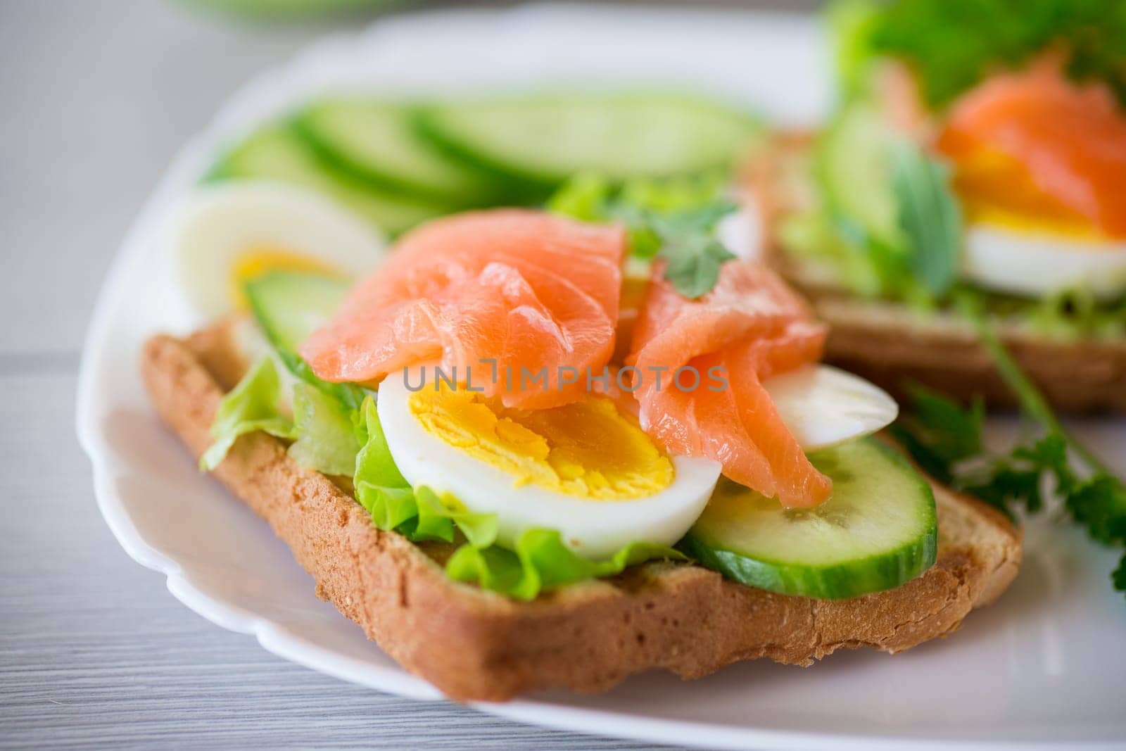 fried toast with lettuce, egg, cucumbers and red fish in a plate, on a wooden table.