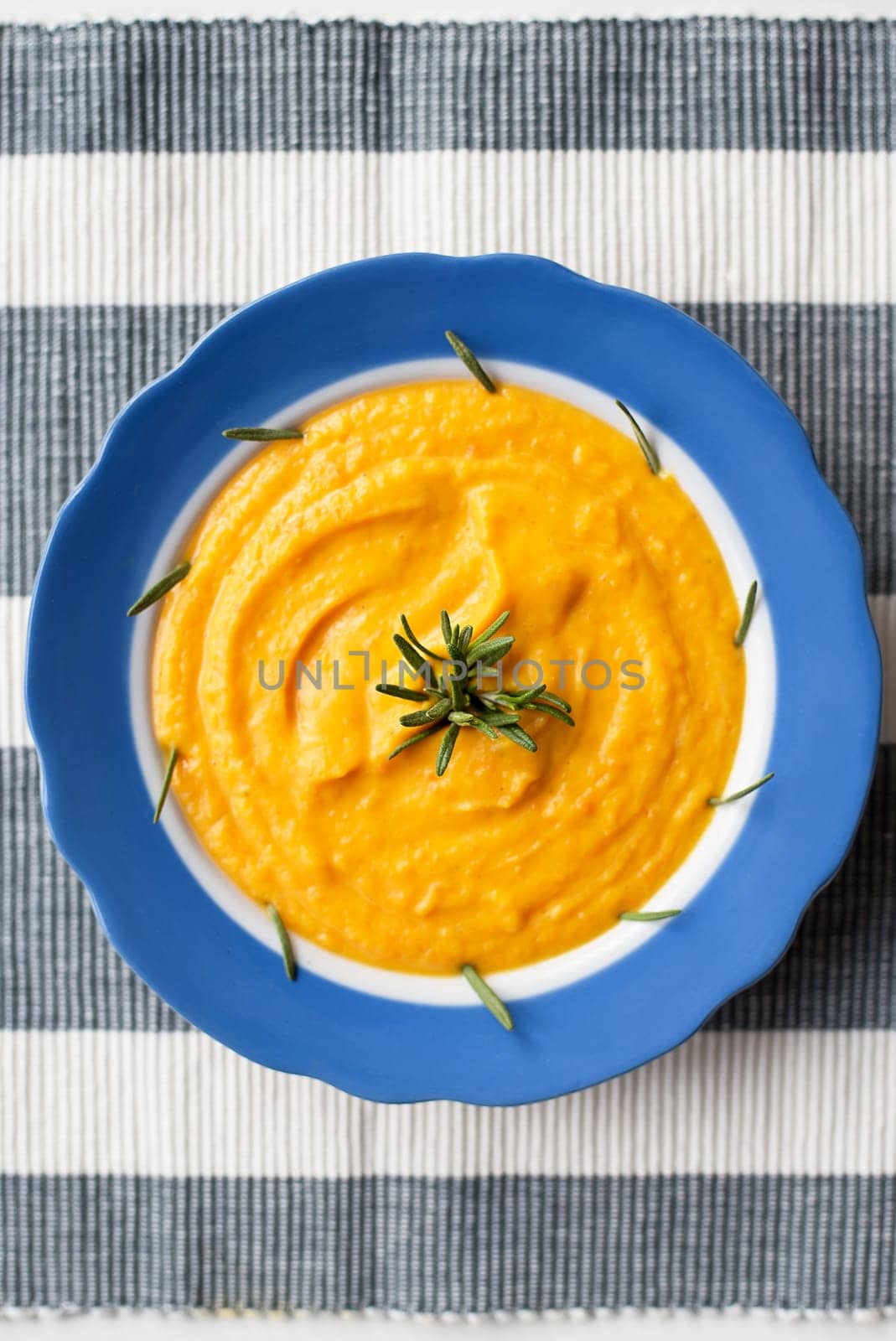 pumpkin cream soup in a blue striped plate on a napkin with rosemary