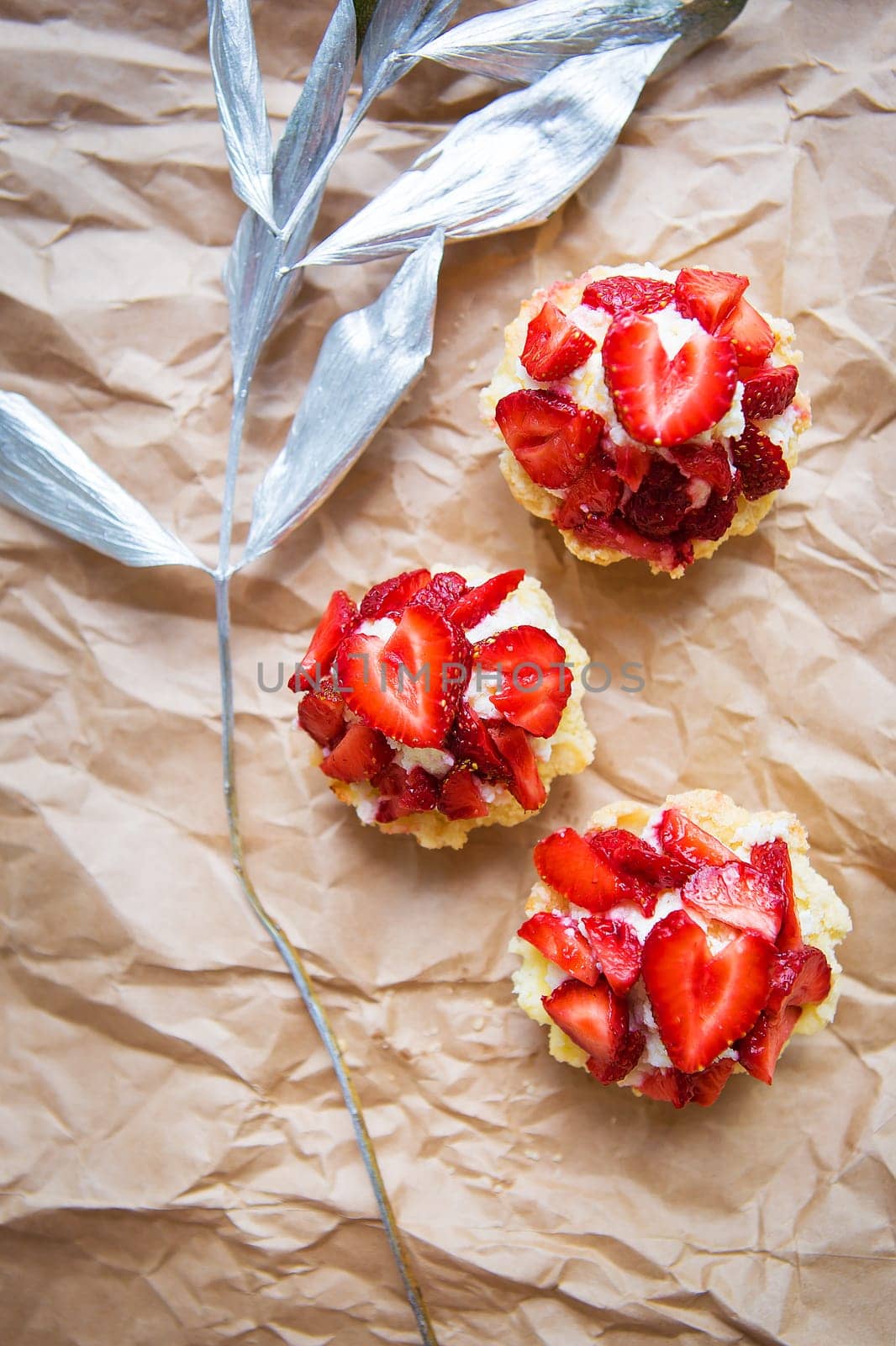 Beautiful cupcakes with strawberries along with a branch on kraft paper by sfinks