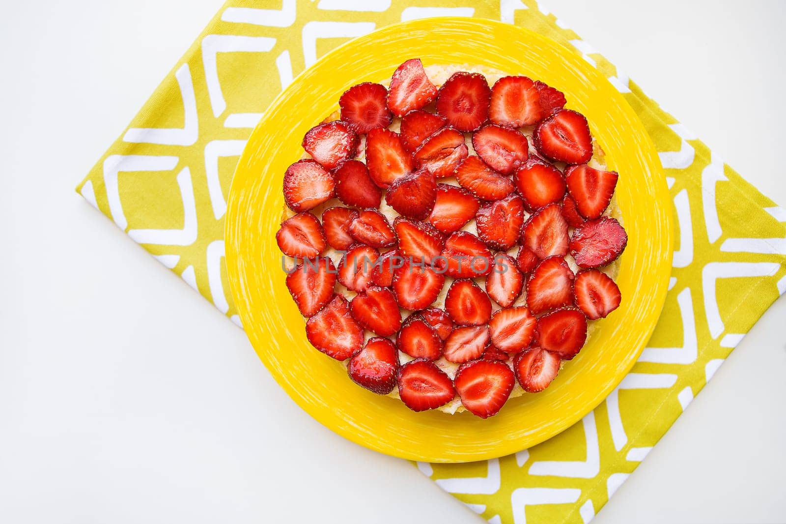 Beautiful and delicious strawberry cake stands on a yellow napkin.