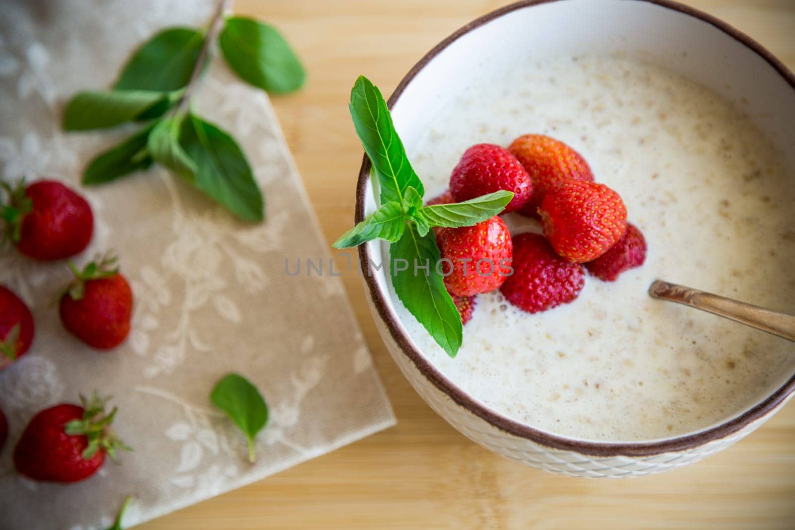 cooked diet oatmeal in a bowl with fresh ripe strawberries, on a wooden table.