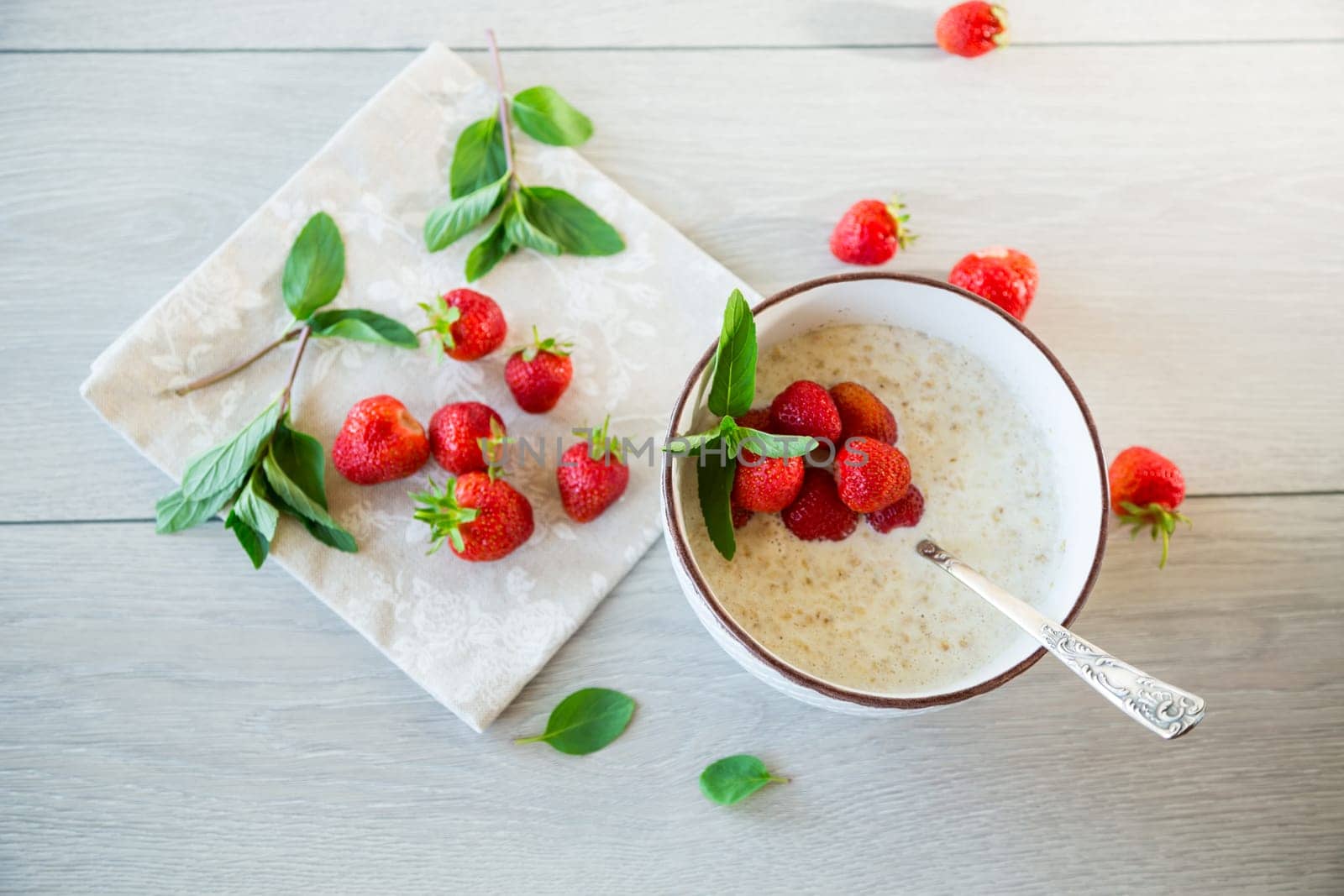 cooked diet oatmeal in a bowl with fresh ripe strawberries, on a wooden table.