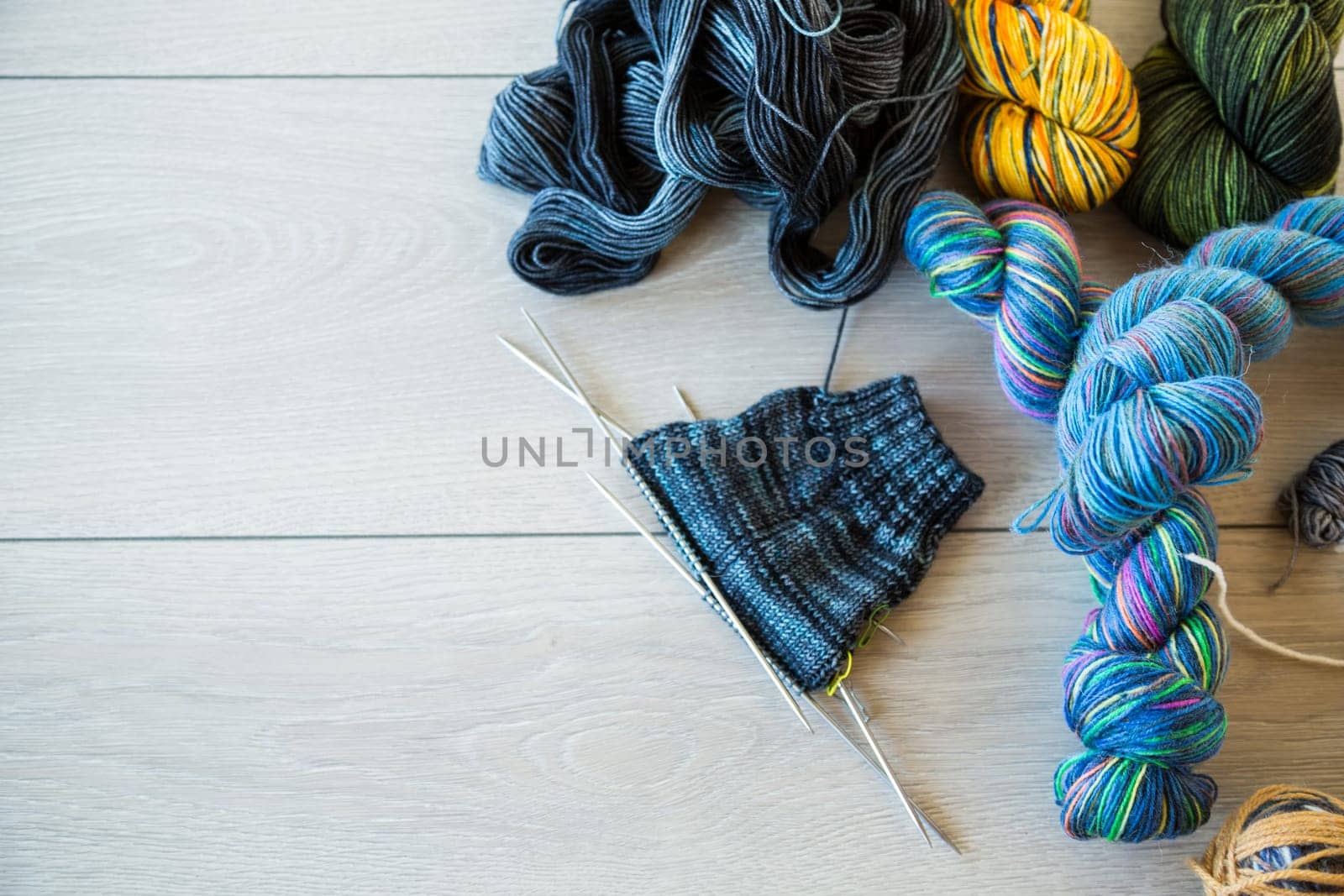 Colored threads, knitting needles and other items for hand knitting, on a light wooden table .