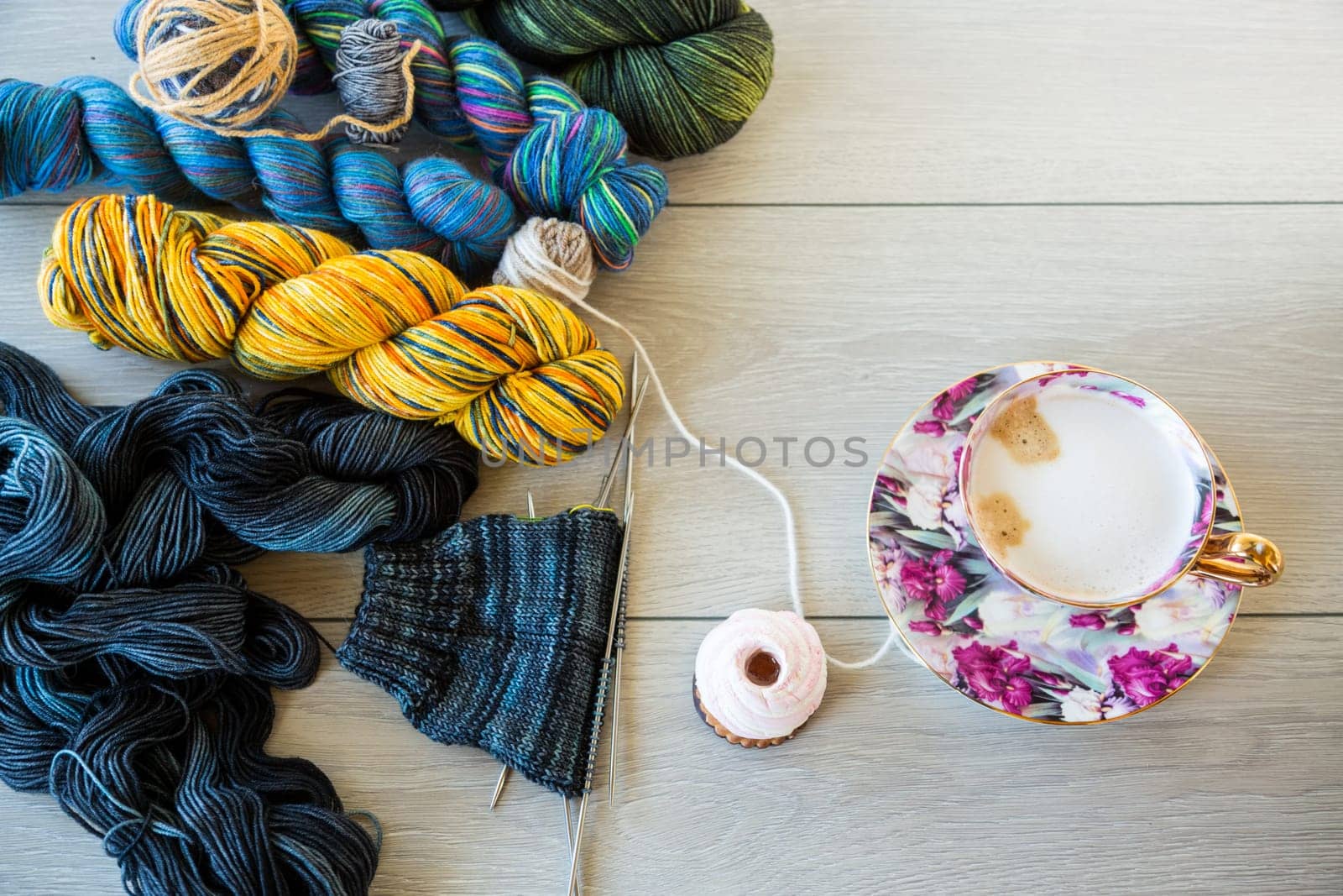 Colored threads, knitting needles and other items for hand knitting, on a light wooden table .