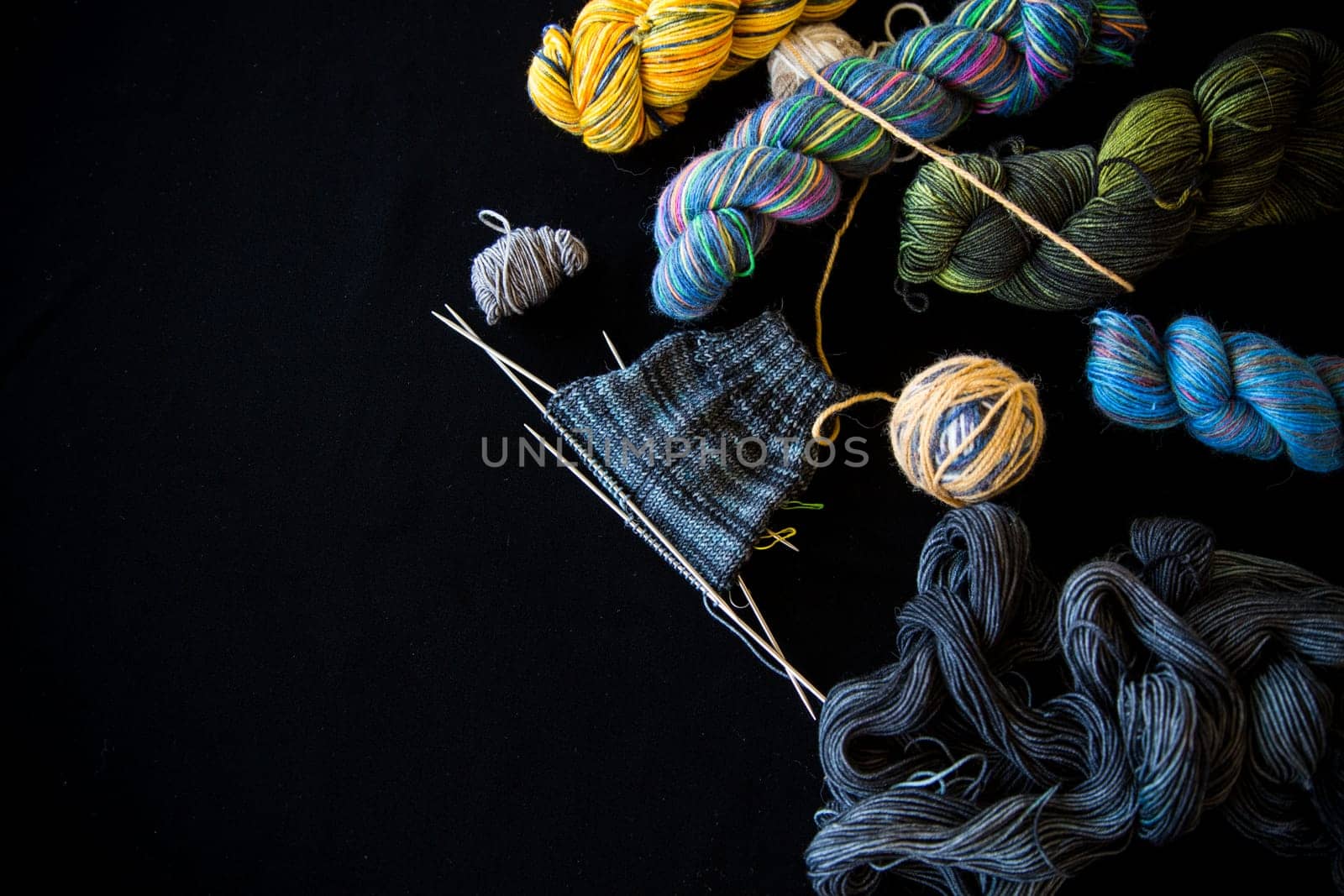 Colored threads, knitting needles and other items for hand knitting, on a black background .