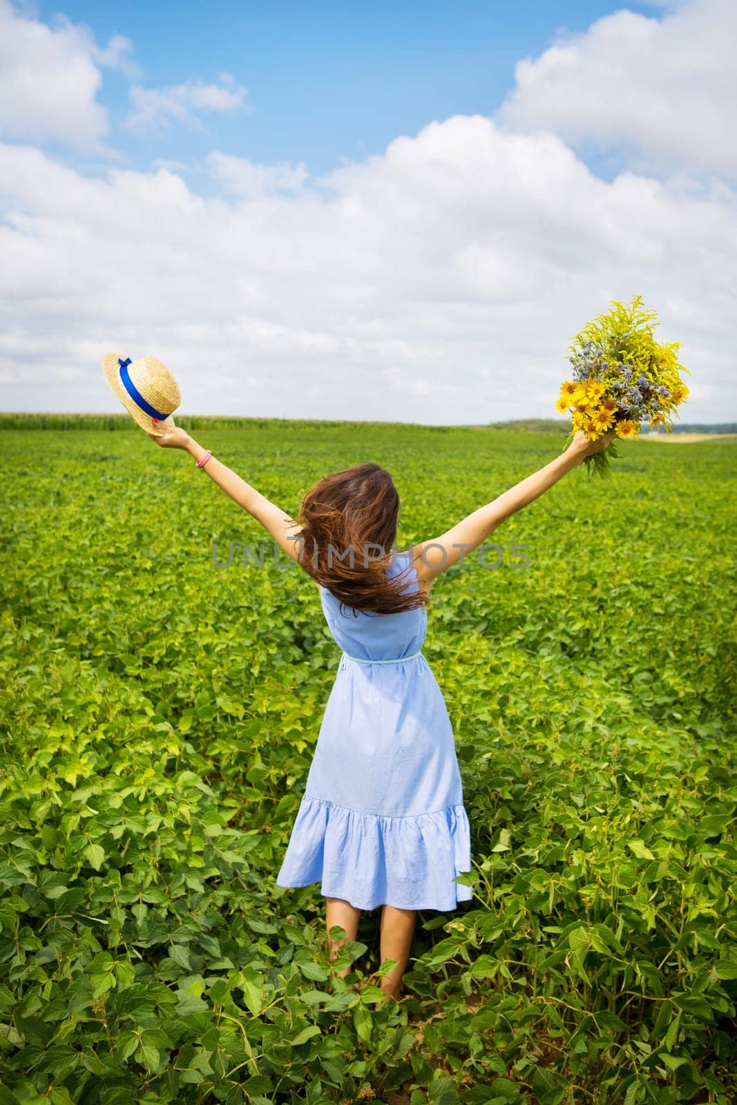 the girl is standing in the field with a bouquet of yellow flowers and a straw hat.