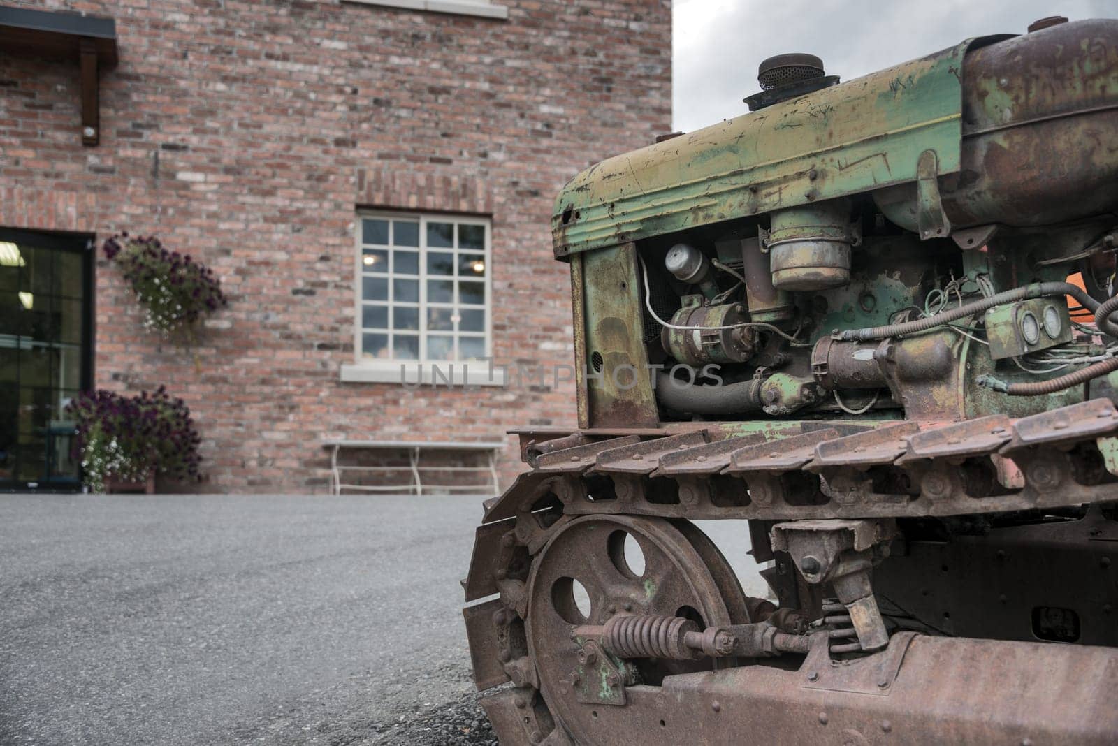 Old rasty tracked tractor in front of brick building by Imagenet