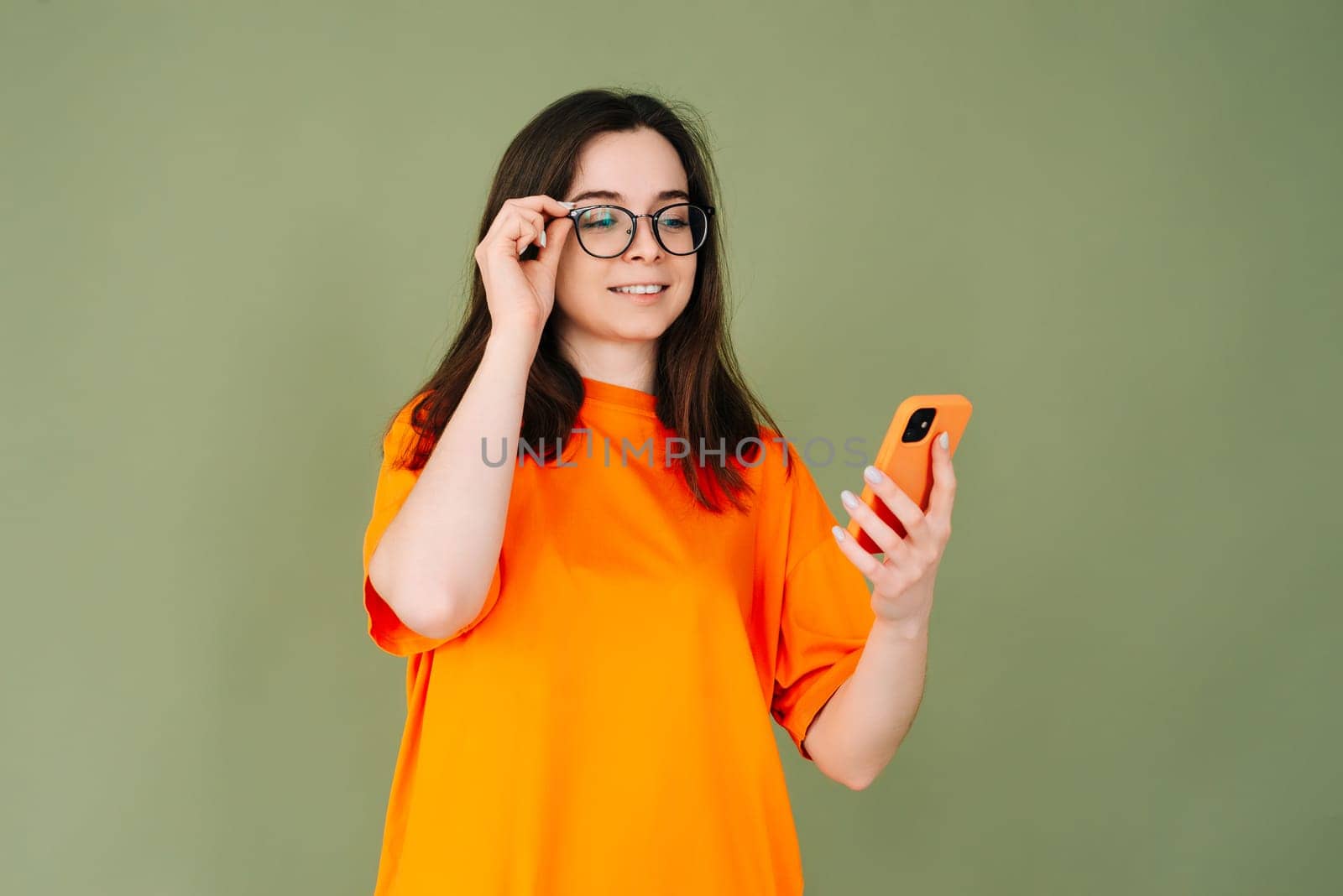 Picture of a cheerful young woman in an orange T-shirt using a modern smartphone in empty green space - technology and communication concept. isolated on green background with copy space for text by ViShark