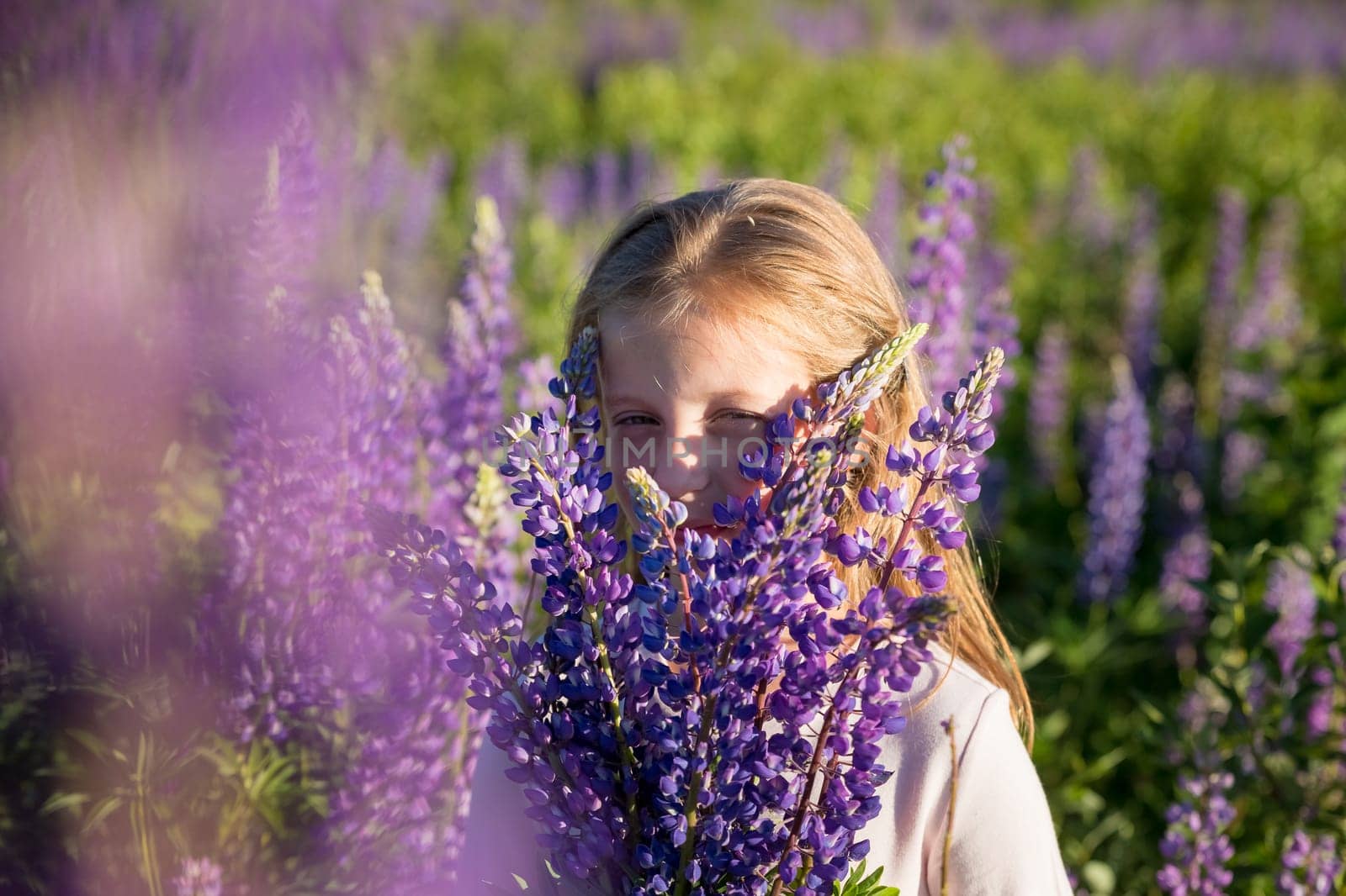 portrait of cute little happy two year old kid girl with bloom flowers lupines in field of purple flowers. nature outdoor.