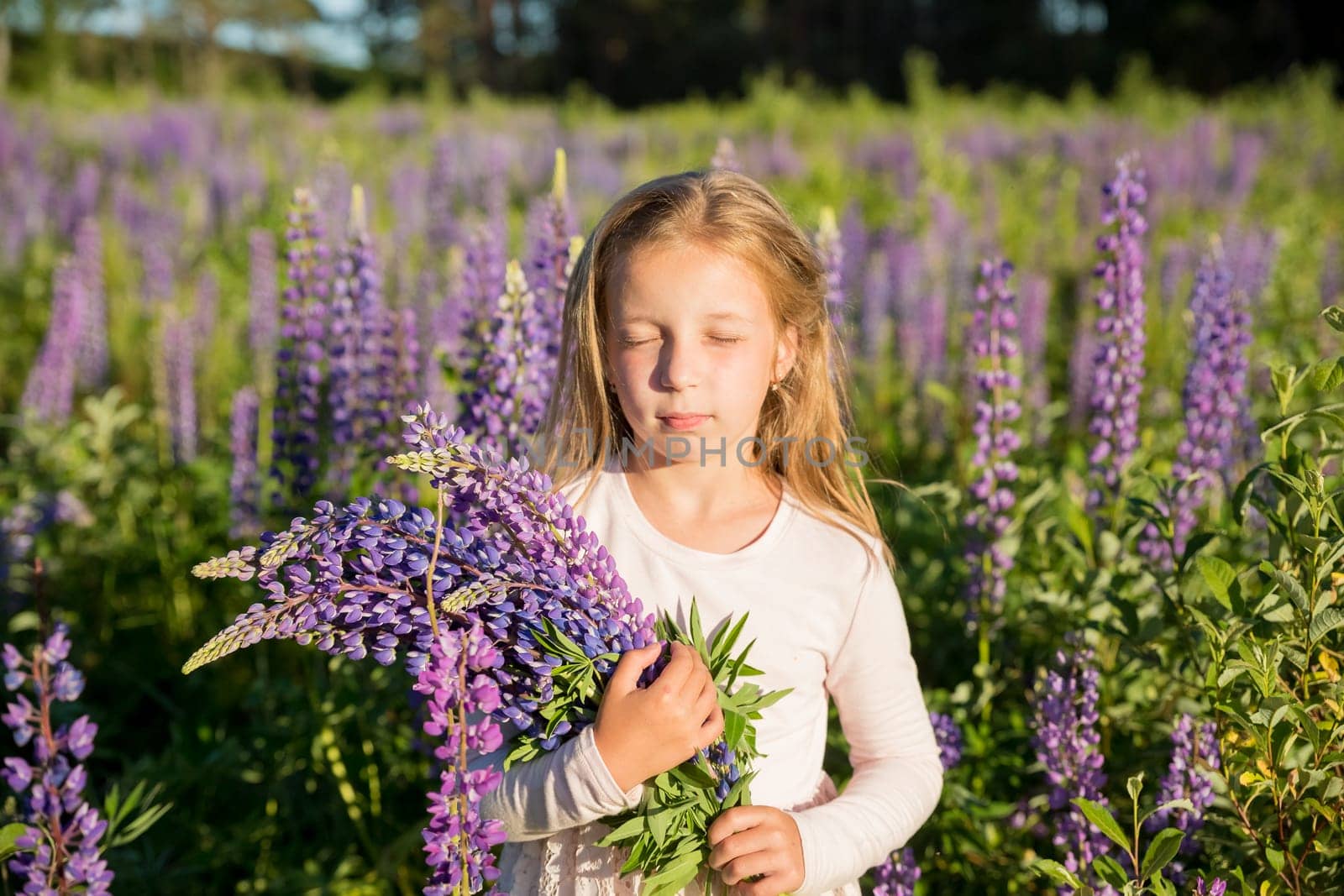 portrait of cute little happy two year old kid girl with bloom flowers lupines in field of purple flowers. nature outdoor.