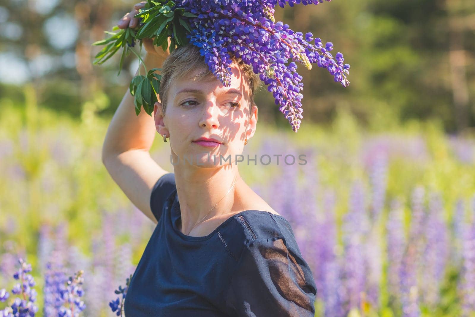 Portrait of young woman holding bouquet of lupin flowers walking in summer meadow.