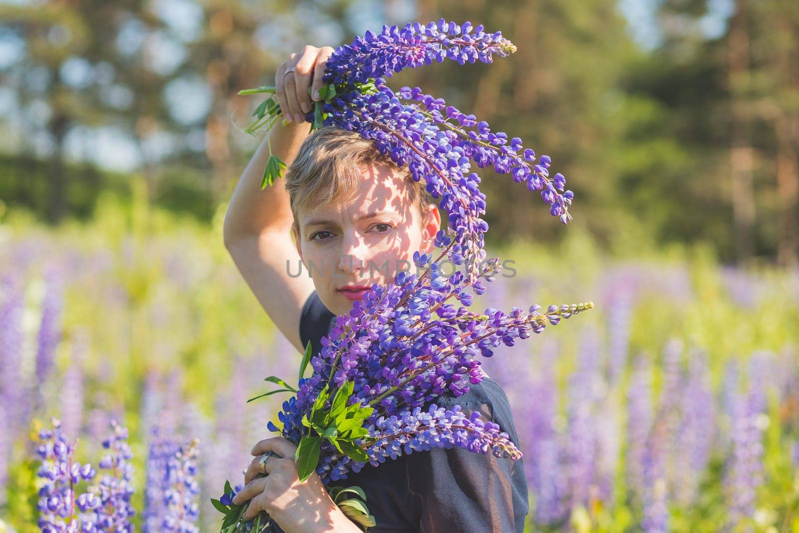 Portrait of young woman holding bouquet of lupin flowers walking in summer meadow.