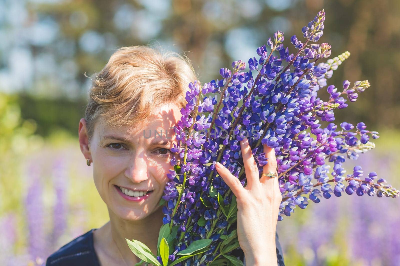 Portrait of young woman holding bouquet of lupin flowers walking in summer meadow.