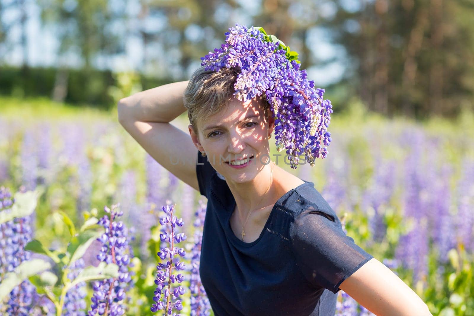 Portrait of young woman holding bouquet of lupin flowers walking in summer meadow.