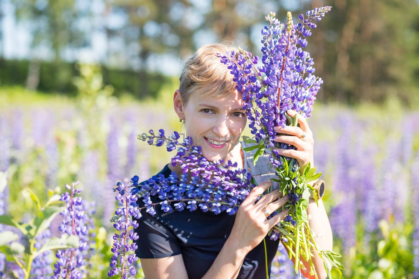 Portrait of young woman holding bouquet of lupin flowers walking in summer meadow.