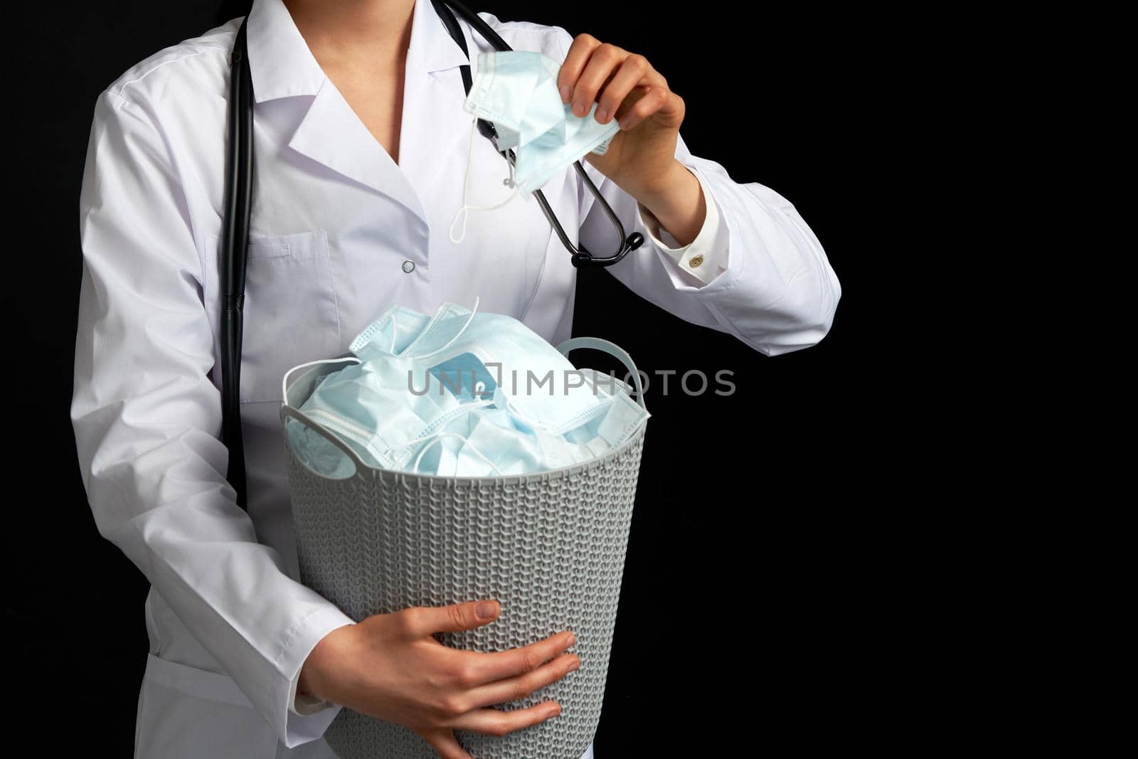 Doctor holding bucket full of used facial masks, virus fight concept with garbage bin