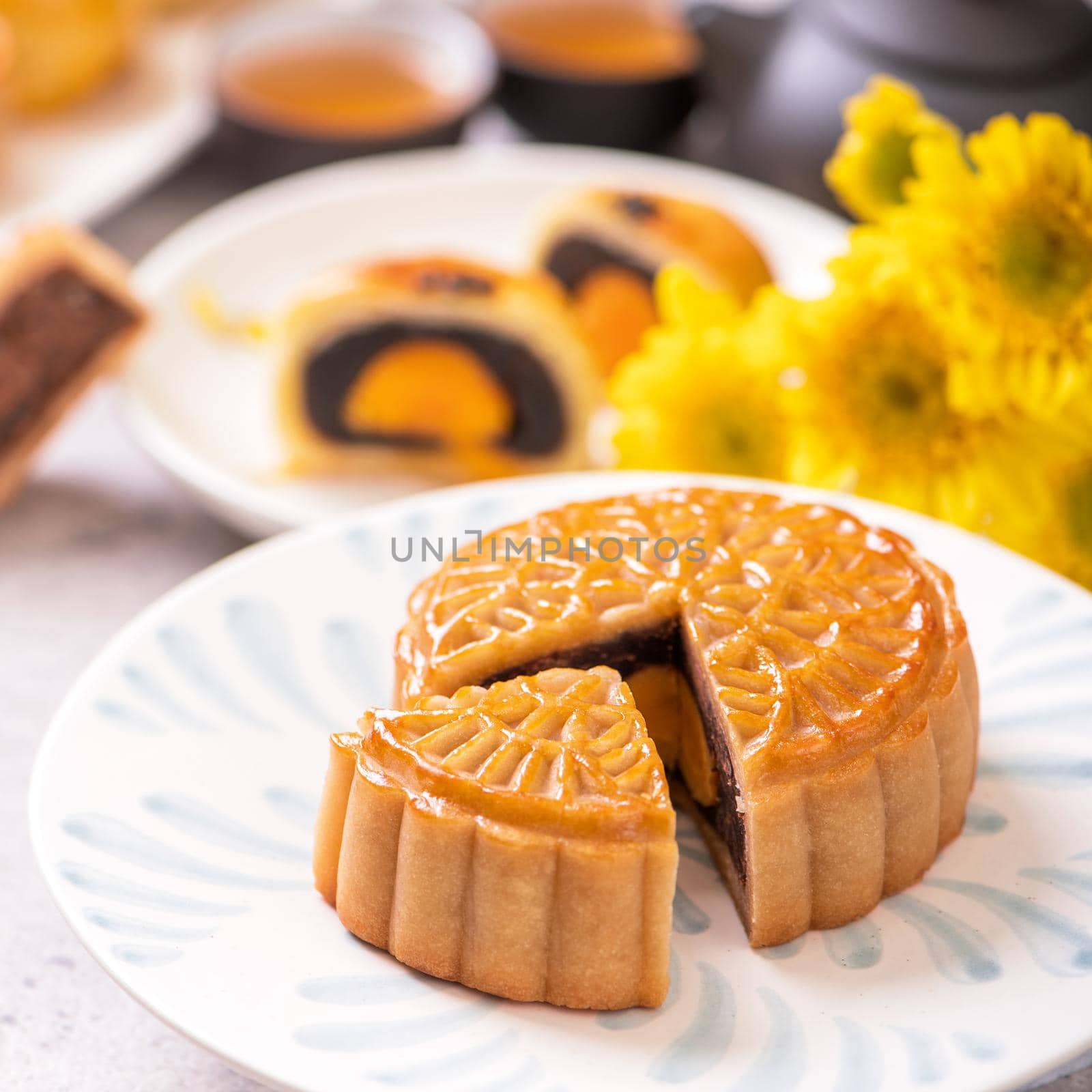 Mid-Autumn Festival traditional food concept - Beautiful cut moon cake on blue pattern plate on white background with flower, close up, copy space