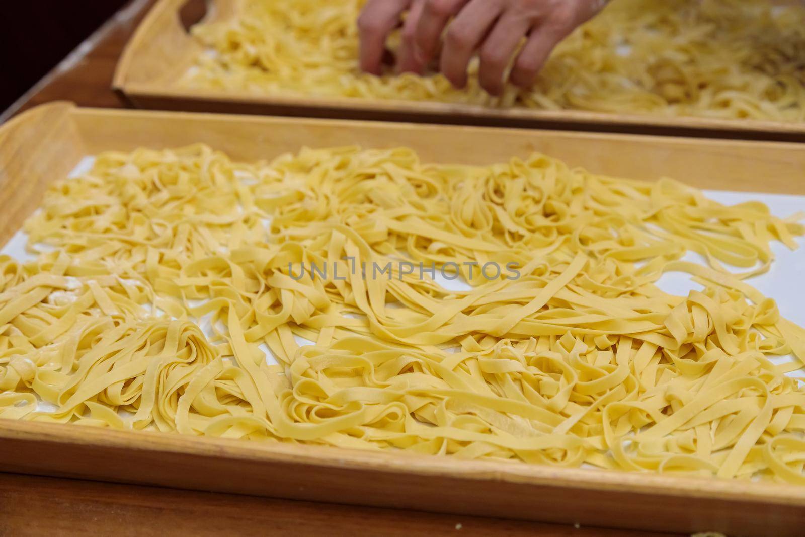 The pasta, cut into long strips, lies on a wooden tray. Use your hands to stir the raw pasta for cooking. Close-up.