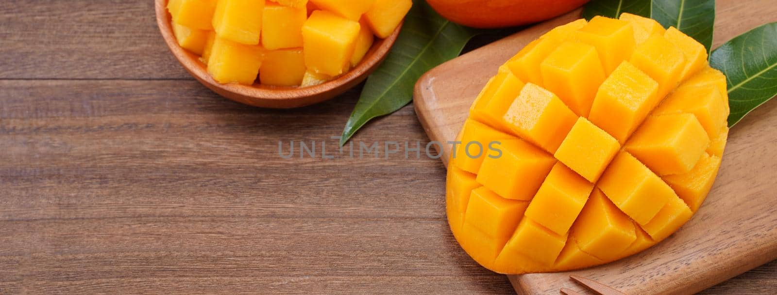 Fresh mango, beautiful chopped fruit with green leaves on dark wooden table background. Tropical fruit design concept. Flat lay. Top view. Copy space