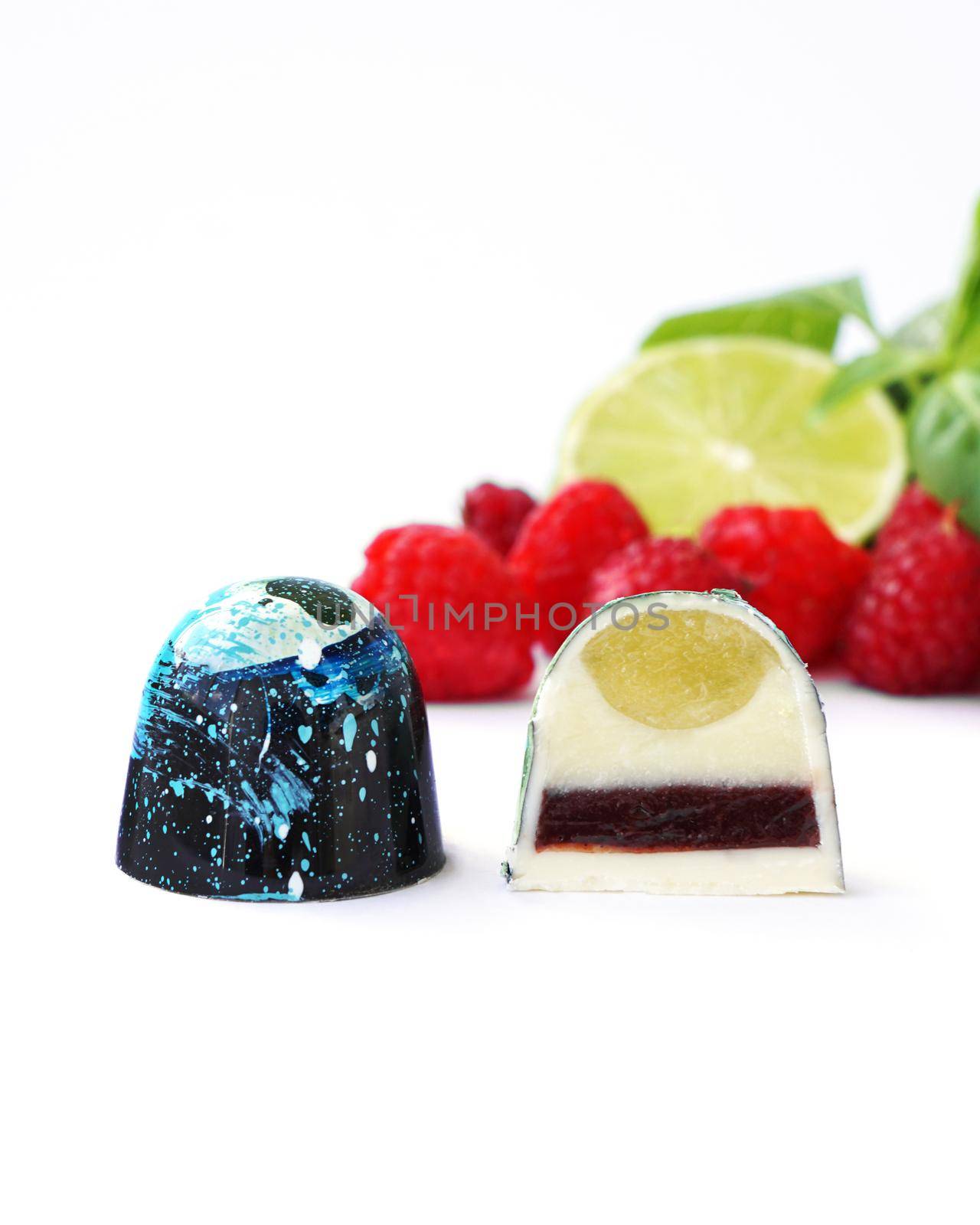 Cutaway chocolate candy. Raspberry, lime and basil on a white background. Handmade sweets.