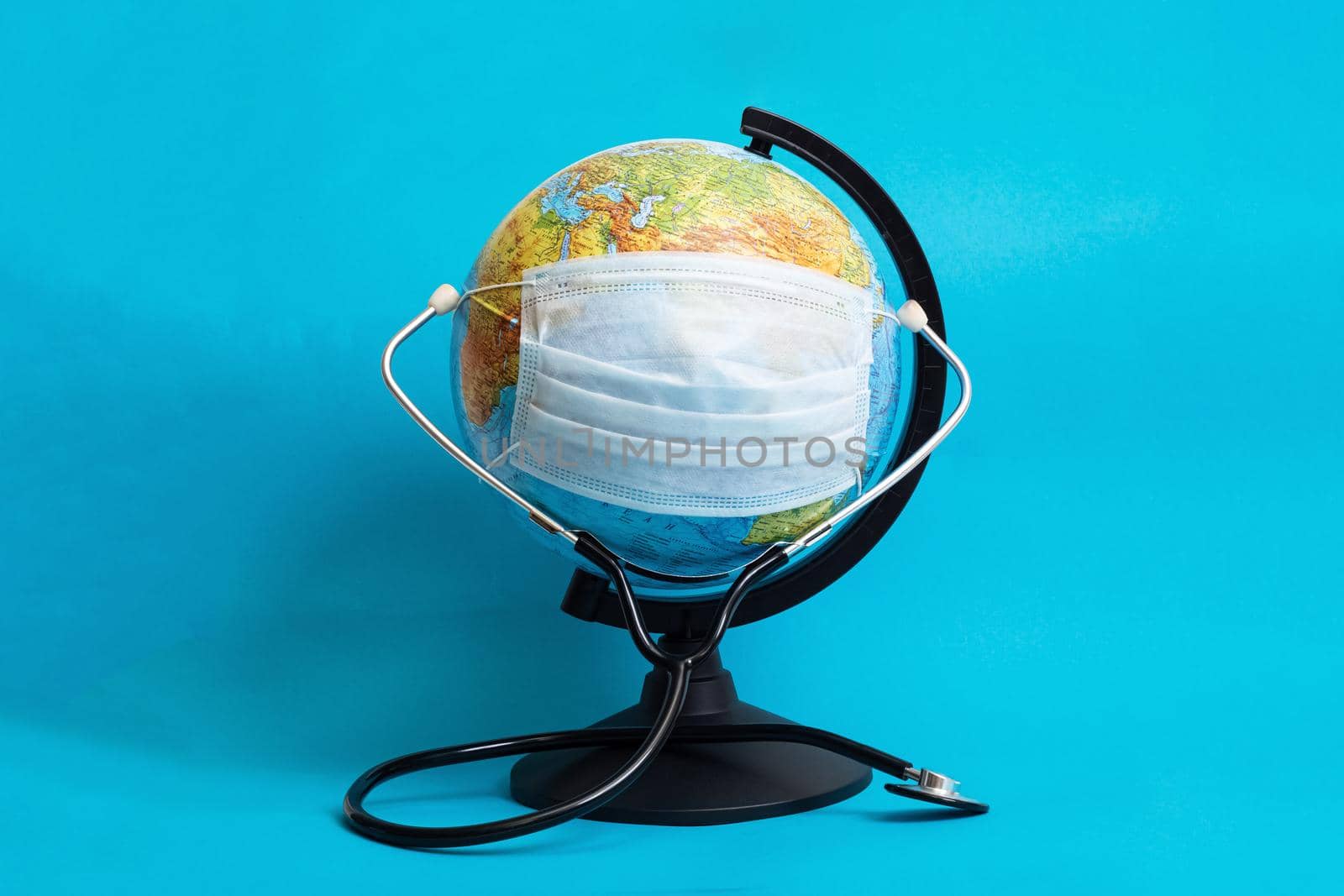 Globe in medical protective mask and stethoscope on blue background close up