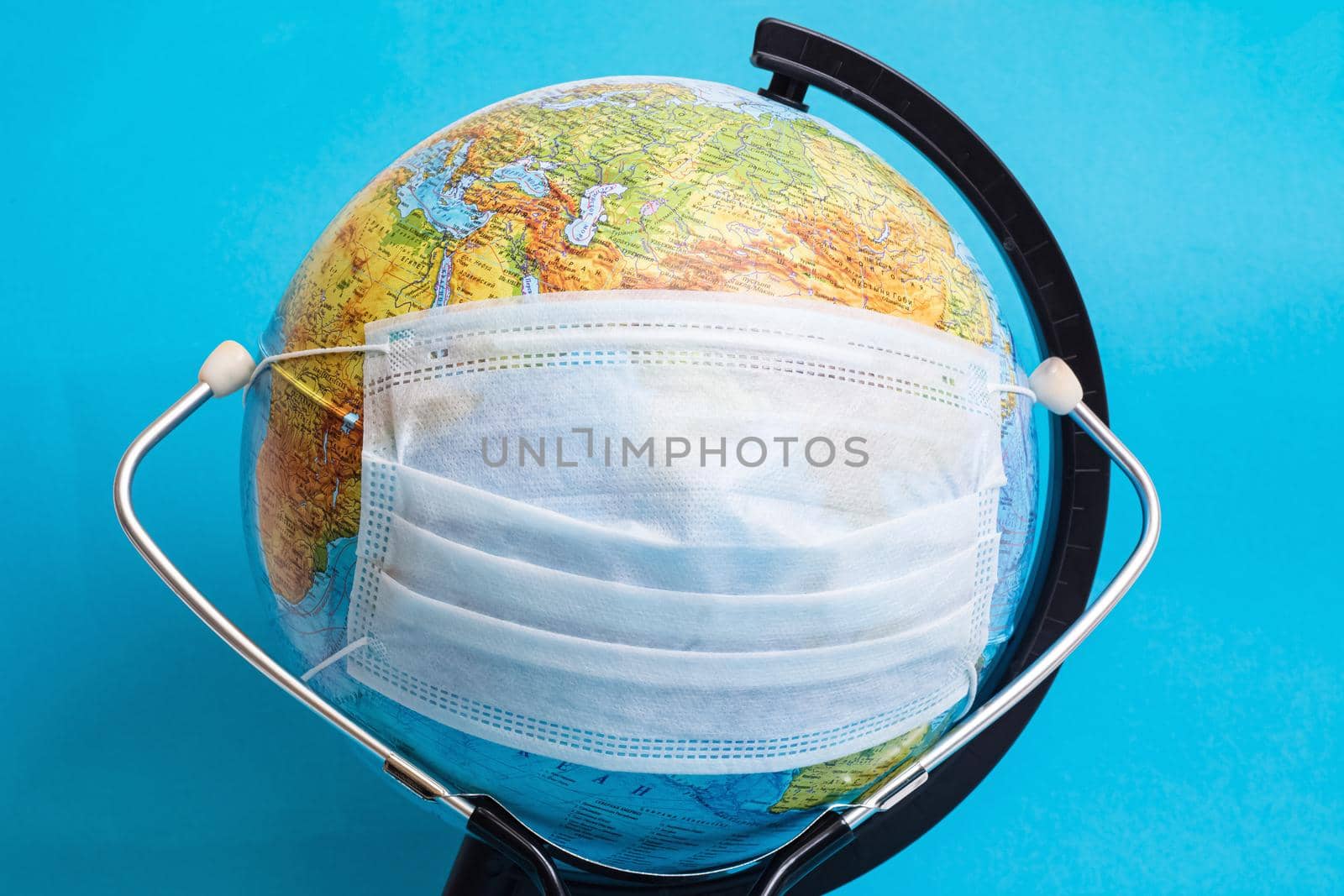 Globe in medical protective mask and stethoscope on blue background close up