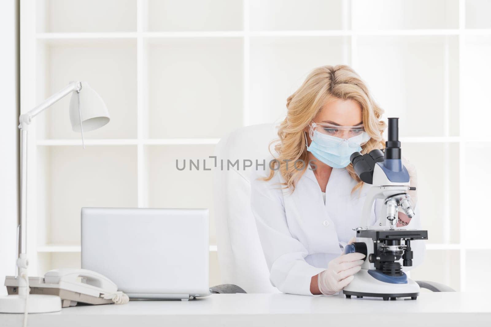 Female doctor looking through a microscope at medical clinic lab