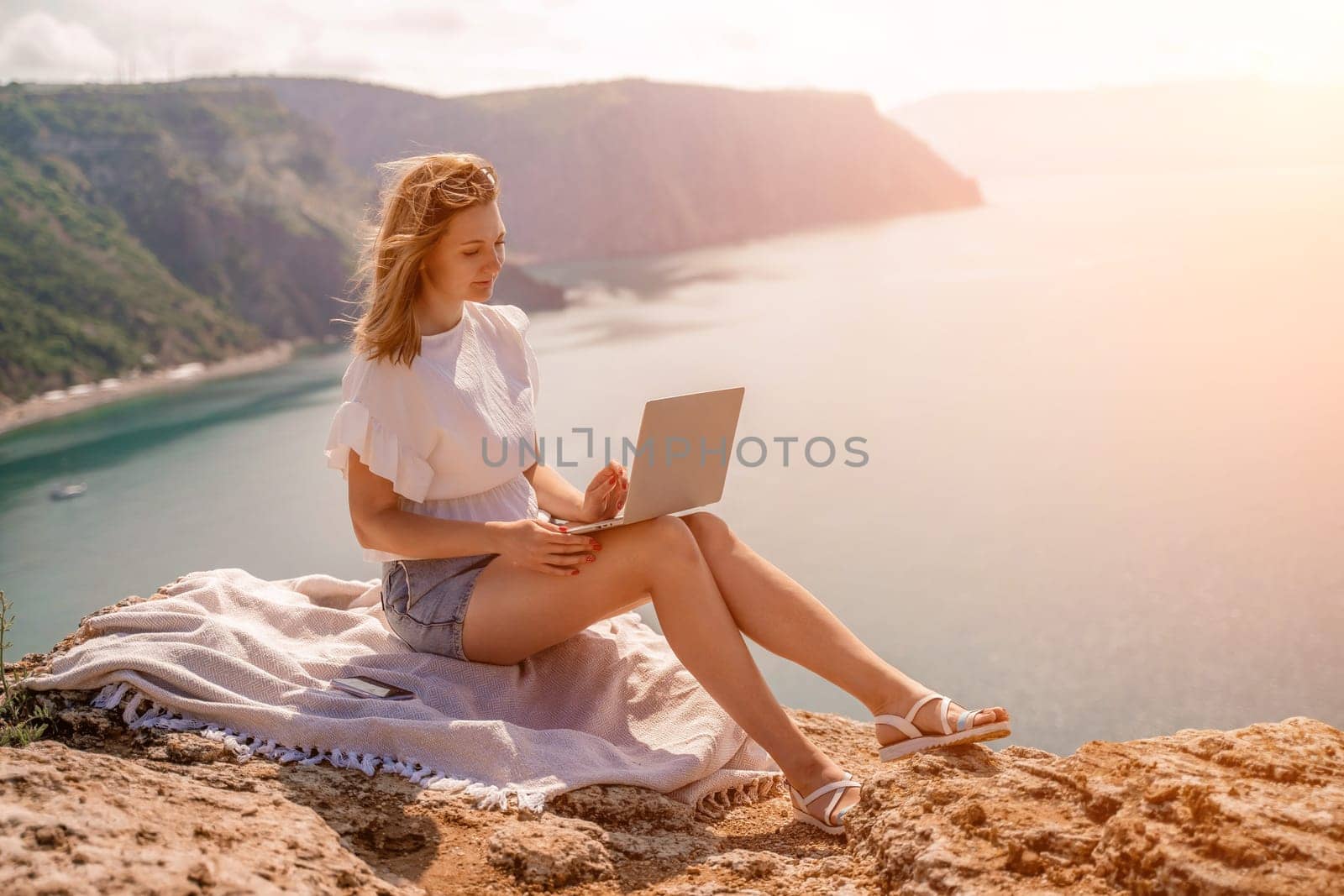 Freelance woman working on a laptop by the sea, typing away on the keyboard while enjoying the beautiful view, highlighting the idea of remote work