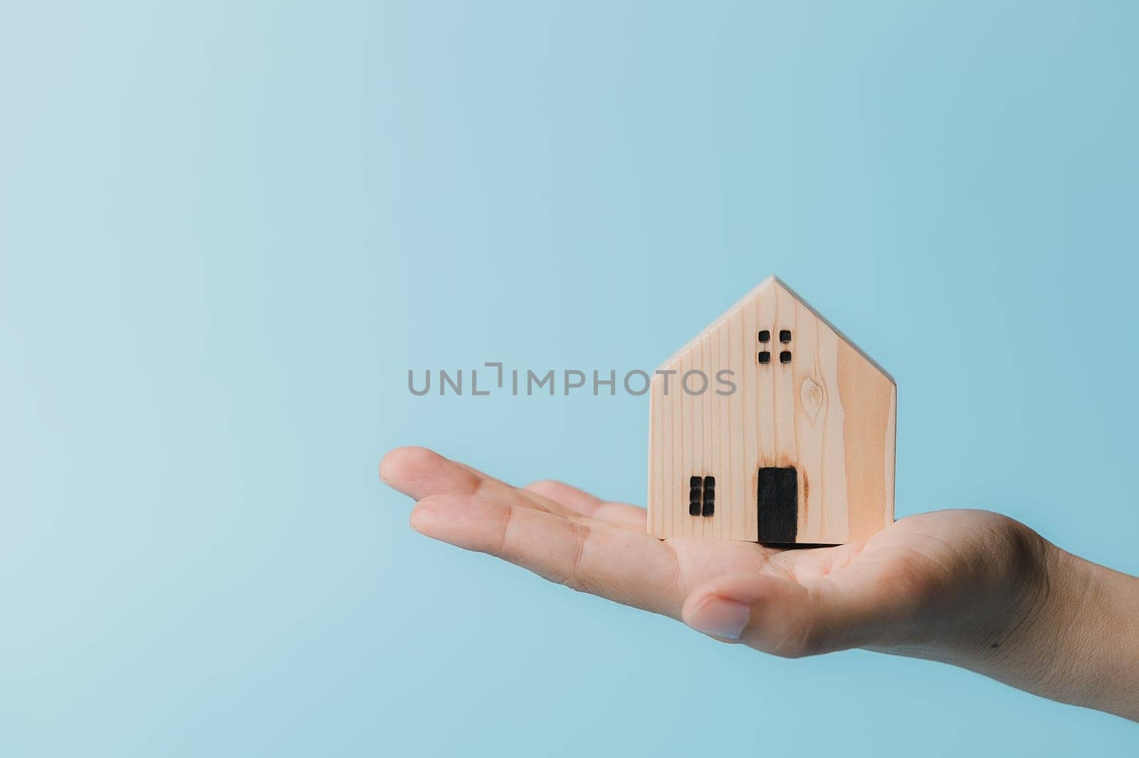 Hand holding a wooden house model on blue background for housing and property concept