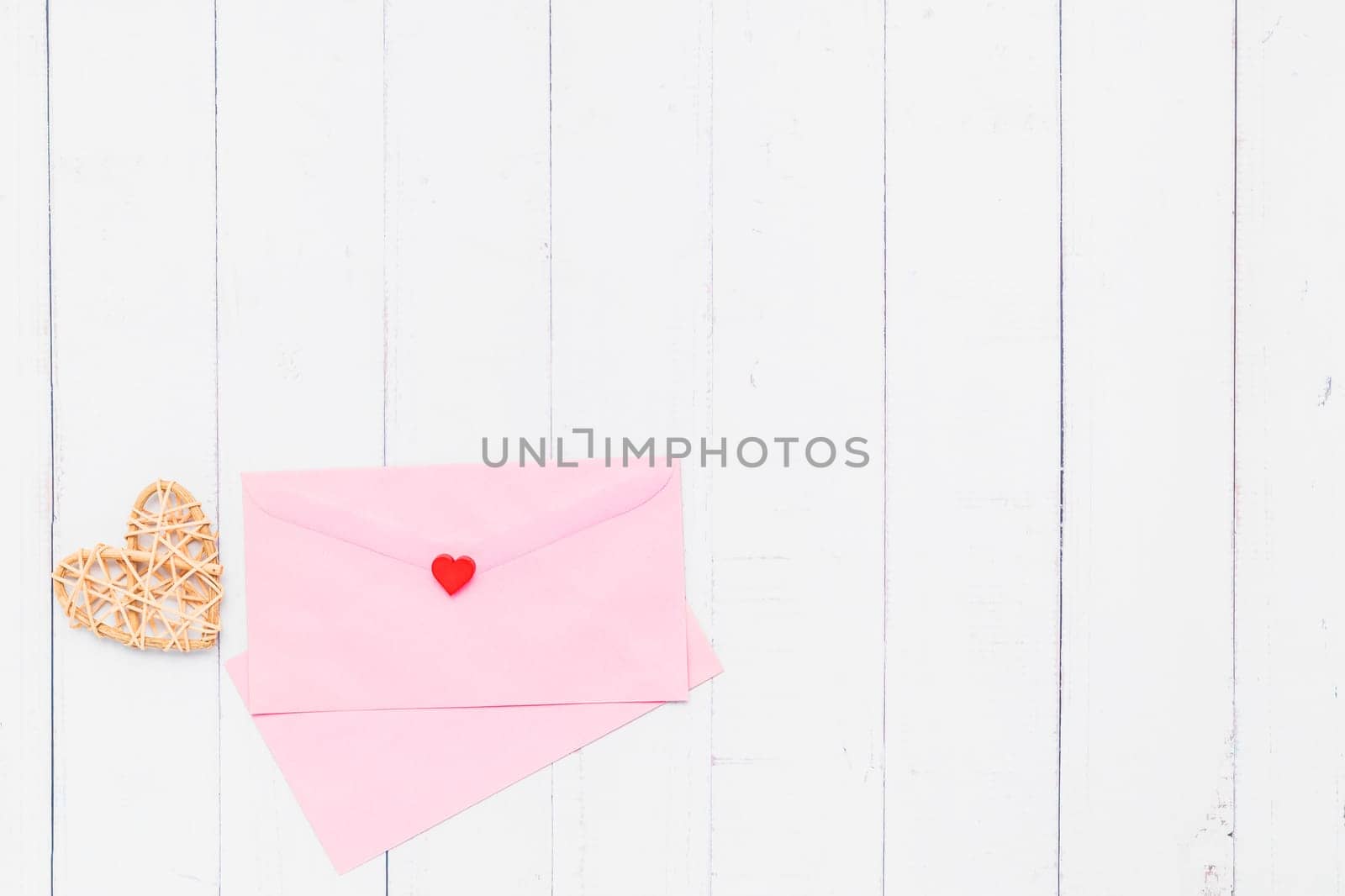 Flat lay of pink envelope with wooden wicker heart on white table background for love and Valentine's day concept